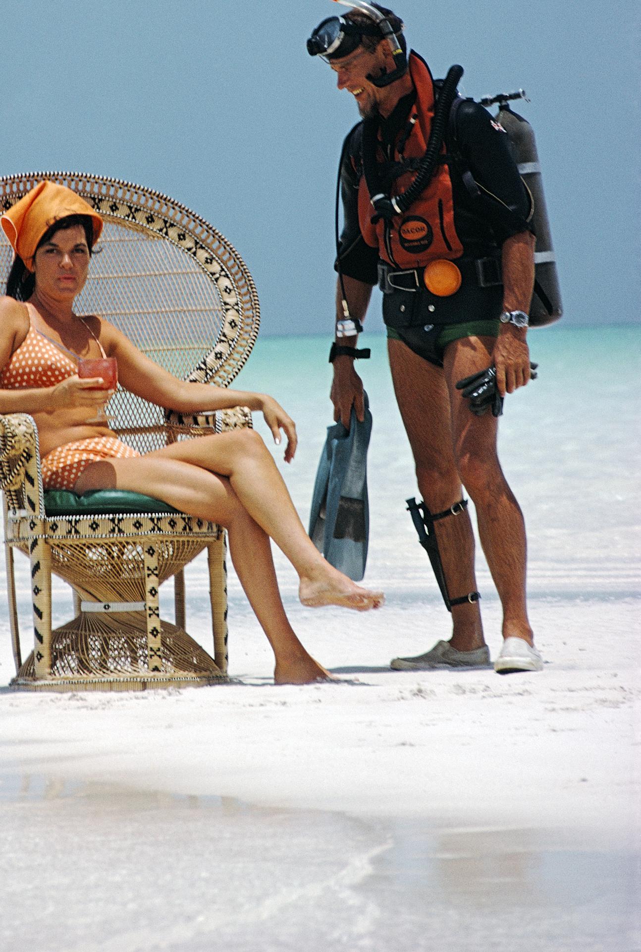 Questo ritratto della fine degli anni '60, scattato dal fotografo di società Slim Aarons, ritrae un uomo con l'attrezzatura da sub che parla con una ragazza su una sedia di vimini sulla spiaggia, alle Bahamas.

Si tratta di un'edizione stampata e