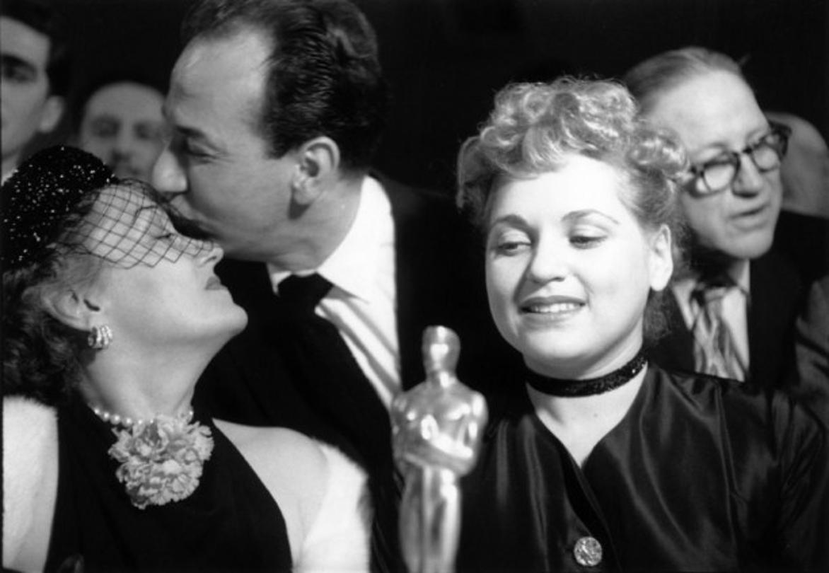 Bad Luck Gloria 
1951
by Slim Aarons

Slim Aarons Limited Estate Edition

American actor Jose Ferrer (1912 – 1992) commiserates with Gloria Swanson after losing out in the contest for the Best Actress oscar, while the winner, Judy Holliday, sits