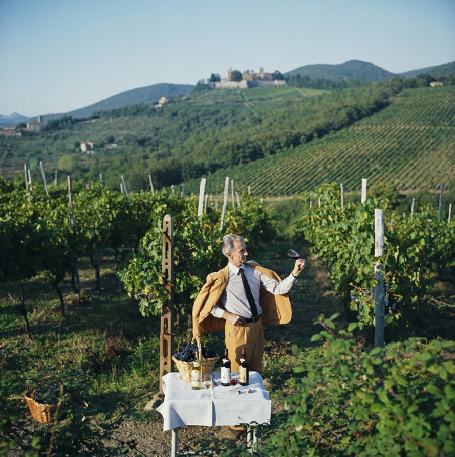 Barone Bettino Ricasoli 
1983
by Slim Aarons

Slim Aarons Limited Estate Edition

Winemaker Barone Bettino Ricasoli poses holding up a wine glass beside a table, on which stands three bottles of wine and a basket of grapes, in a vineyard in Siena,