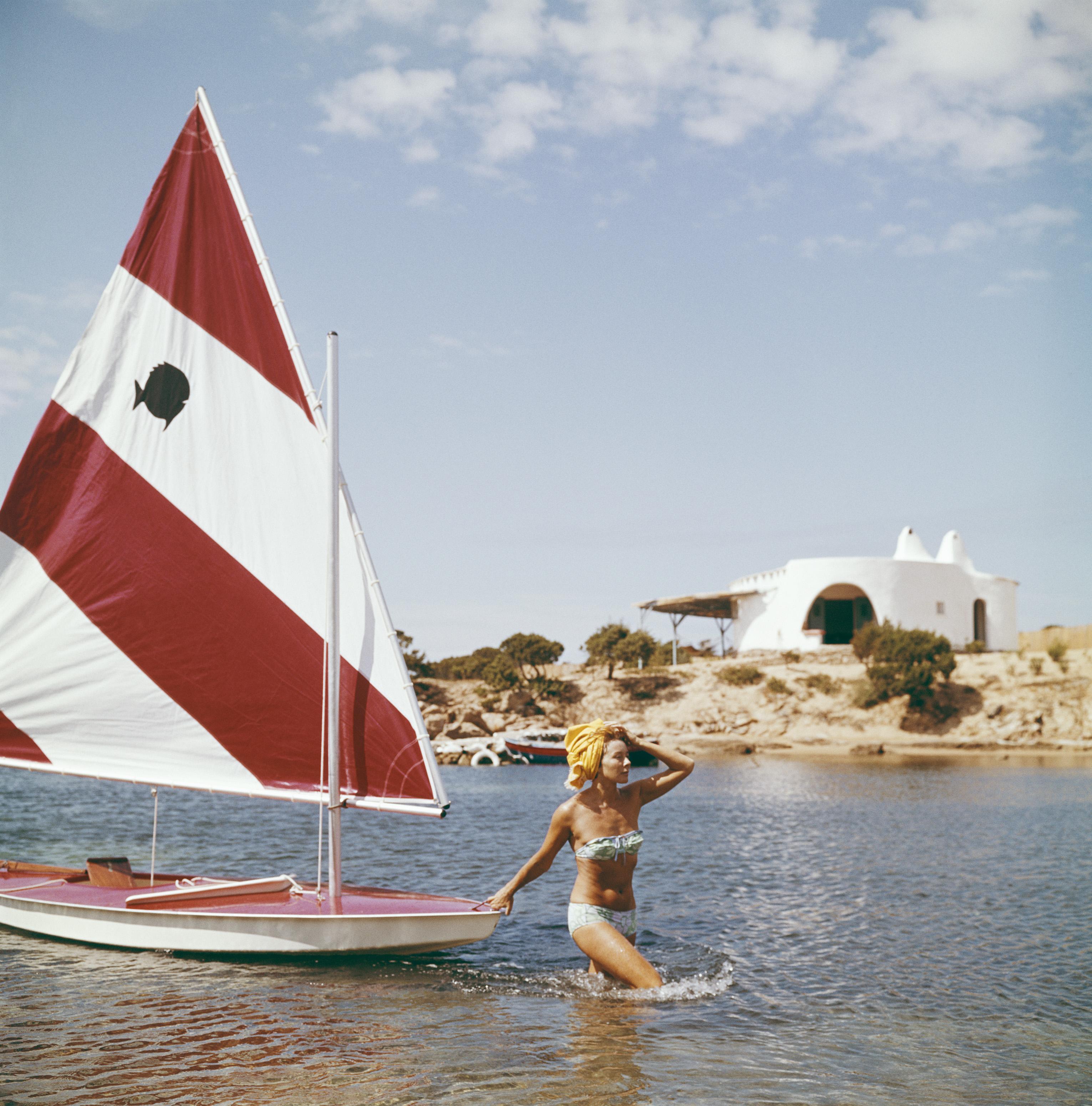 Slim Aarons Landscape Photograph - Bettina Graziani with a small yacht, Costa Smeralda, Sardinia, Italy, Estate Ed.