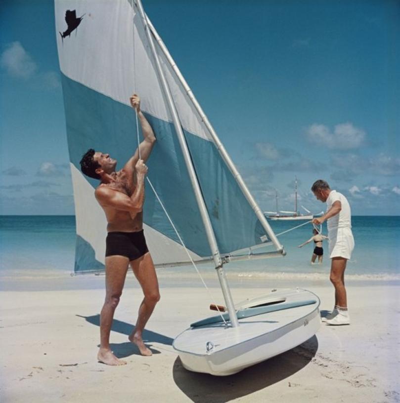 Boating In Antigua 
1961
by Slim Aarons

Slim Aarons Limited Estate Edition

American actor Hugh O’Brian (left) hoists the sail on a dinghy, Antigua, West Indies, 1961.

unframed
c type print
printed 2023
16×16 inches - paper size


Limited to 150