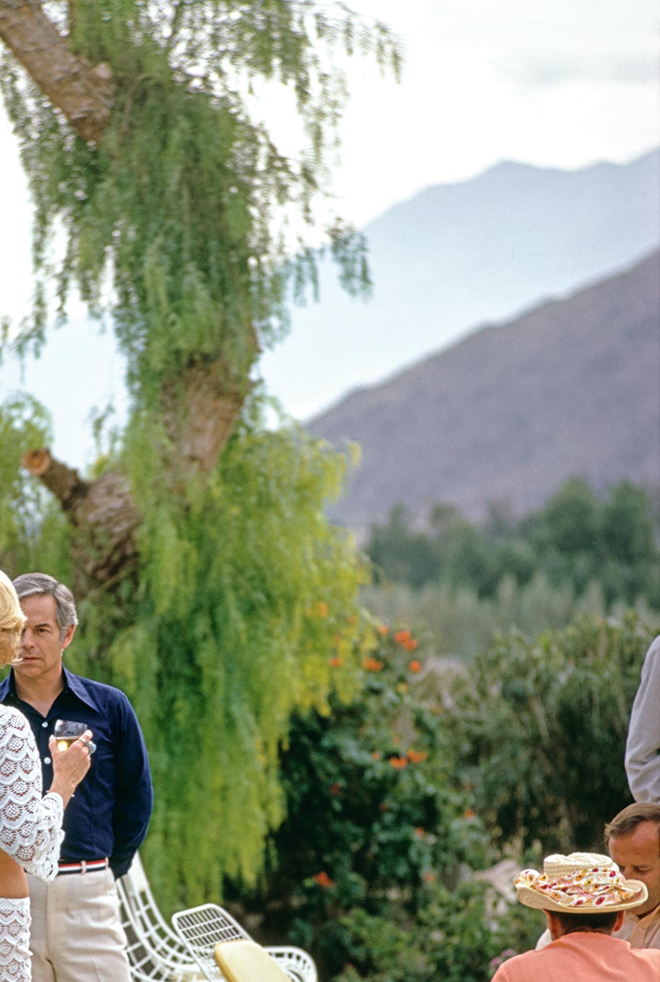 Dieses Porträtfoto aus dem Jahr 1970, aufgenommen von dem Society-Fotografen Slim Aarons, zeigt das ehemalige Fotomodell Helen Dzo Dzo (in weißer Häkelarbeit, links) im Gespräch mit einem Gast am Pool des Wüstenhauses von Nelda Linsk in Palm