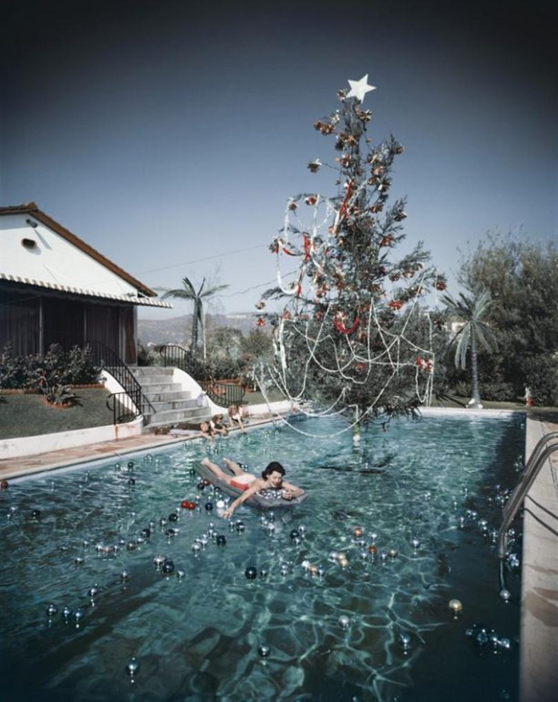 Christmas Swim 
1956
by Slim Aarons

Slim Aarons Limited Estate Edition

Rita Aarons, wife of photographer Slim Aarons, swimming in a pool festooned with floating baubles and a decorated Christmas tree, Hollywood, California, 1954. Two children play