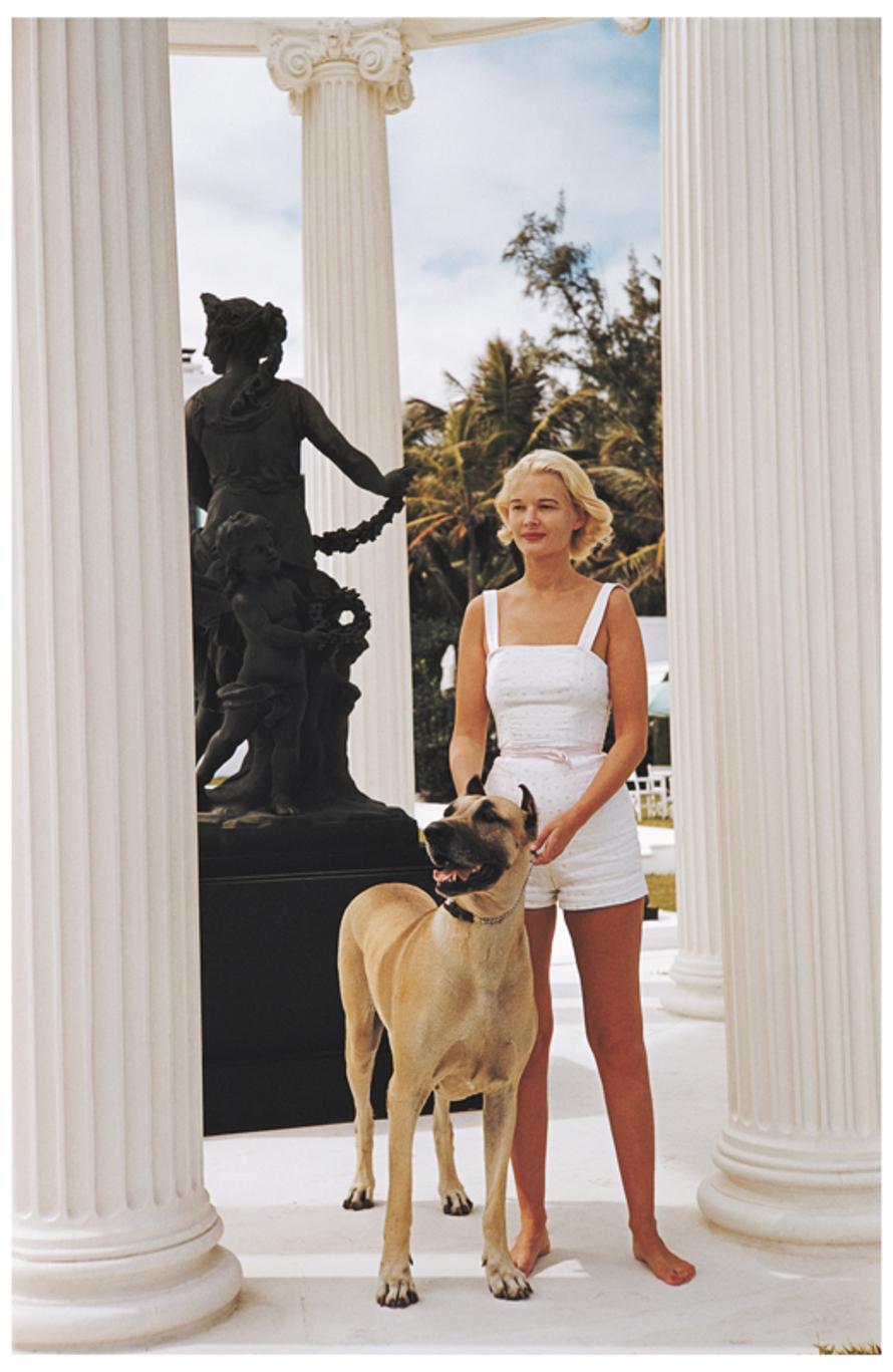 CZ Guest With Her Great Dane 
1955
by Slim Aarons

Slim Aarons Limited Estate Edition

American socialite C.Z. Guest (Mrs Winston F.C. Guest) (1920 – 2003) with a large Great Dane dog, at her Grecian temple pool on the ocean-front estate, Villa