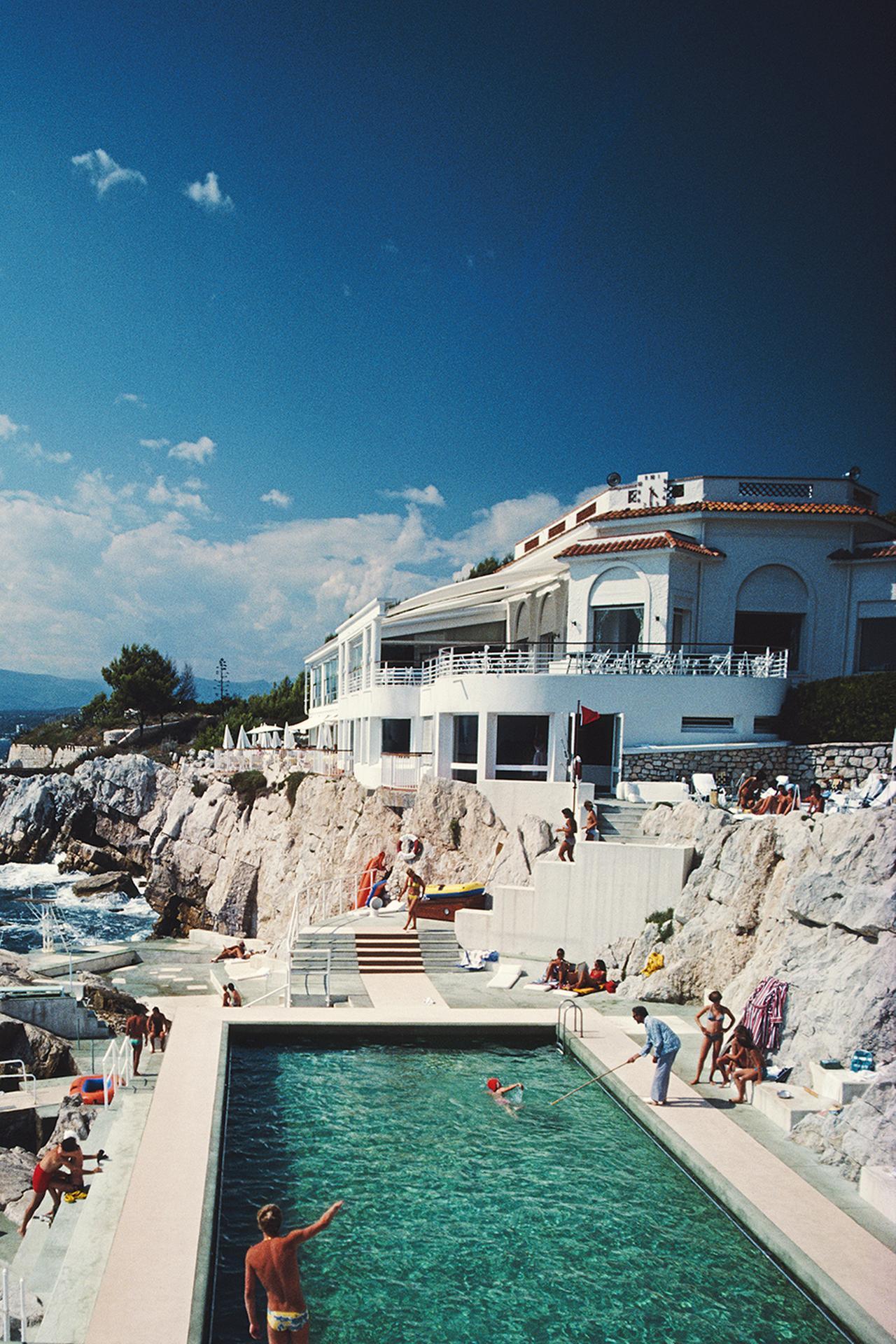 Cette photographie du milieu des années 1970, prise par le photographe mondain Slim Aarons, montre des clients autour de la piscine de l'hôtel du CAP Eden-Roc, à Antibes, en France, 

Il s'agit d'une édition de 150 exemplaires estampillés et