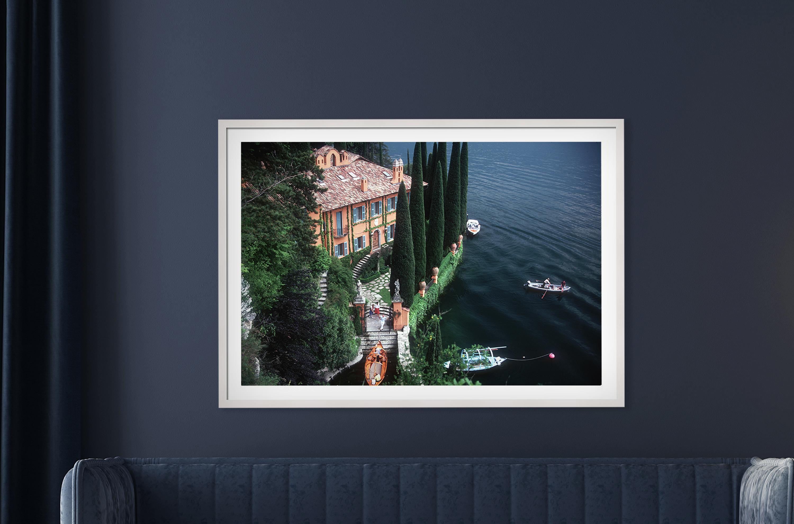 Giacomo and Stefania Mantegazza welcome guests arriving by boat at their villa, La Casinella, on Lake Como, 1983. Brilliant green trees contrast with the vivid orange, reds and turquoise of the architecture. Four boats can are afloat on the deep
