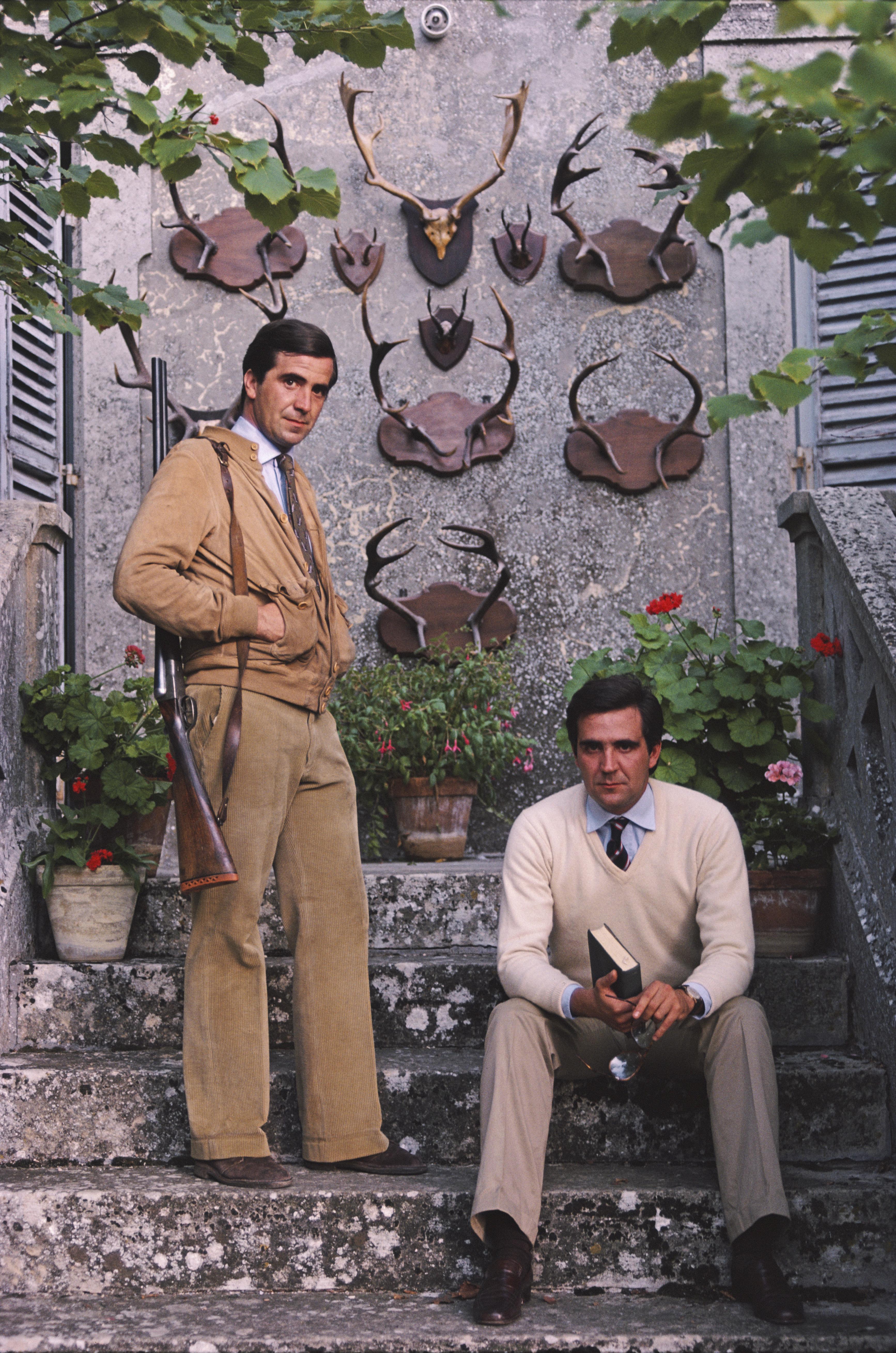 'Gioacchino And Gian Nicola Fiilippi' 1982 Slim Aarons Limited Estate Edition Print 

Gioacchino and Gian Nicola Fiilippi pose before a display of antlers mounted on the wall behind them in San Marino, in September 1982. One carries a rifle over his