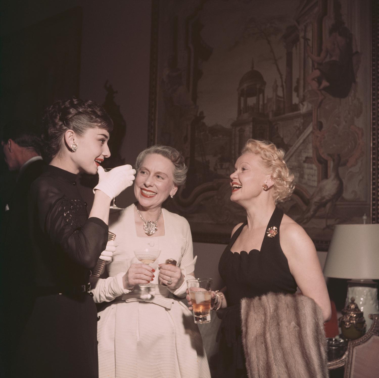 On the left film star Audrey Hepburn (1929 - 1993) talks with Mrs Grover Magnin (centre) and another guest at a party in San Francisco, 1953.

The beautiful and fashionable movie star and style icon dressed in her eponymous look; all in black with