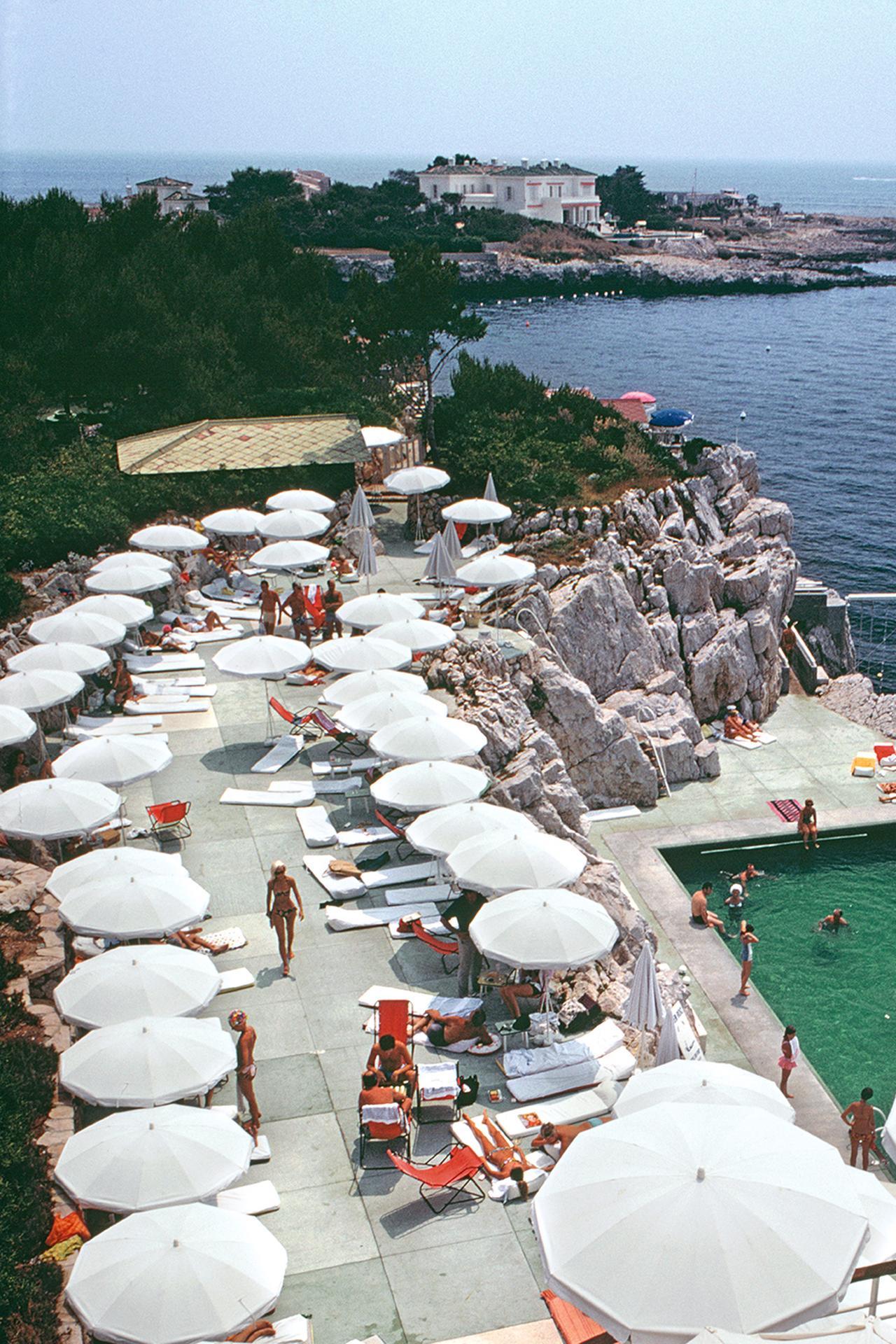 This late 1960s landscape photograph, captured by society photographer Slim Aarons, features guests round the swimming pool at the Hotel du Cap Eden-Roc, Antibes, France, August.

This is an estate stamped and hand numbered edition of 150 with