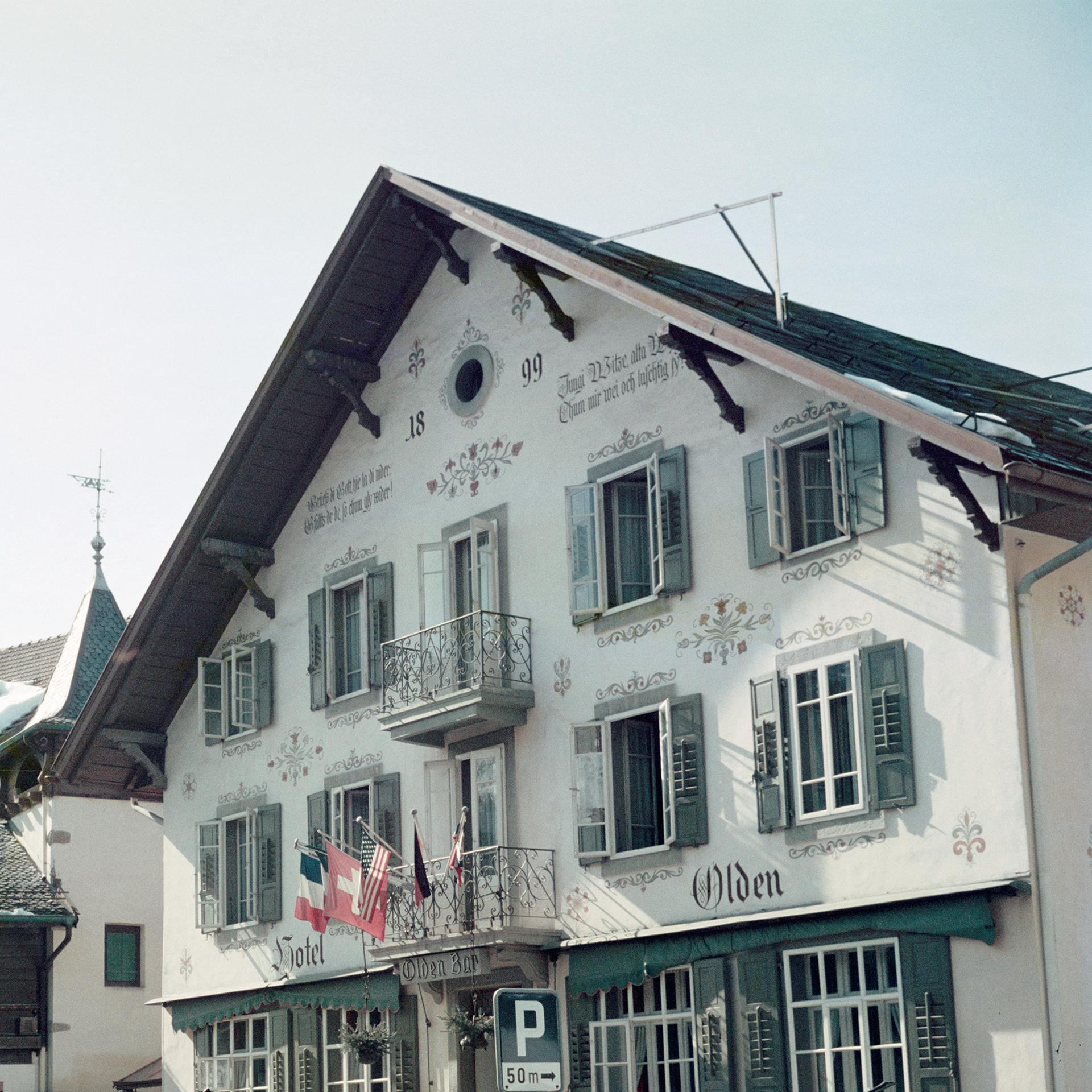 Questa fotografia urbana dei primi anni '60, scattata dal fotografo di società Slim Aarons, ritrae delle persone che portano gli sci davanti all'Hotel Olden di Gstaad, nel 1961. 

Si tratta di un'edizione stampata e numerata a mano di 150 esemplari