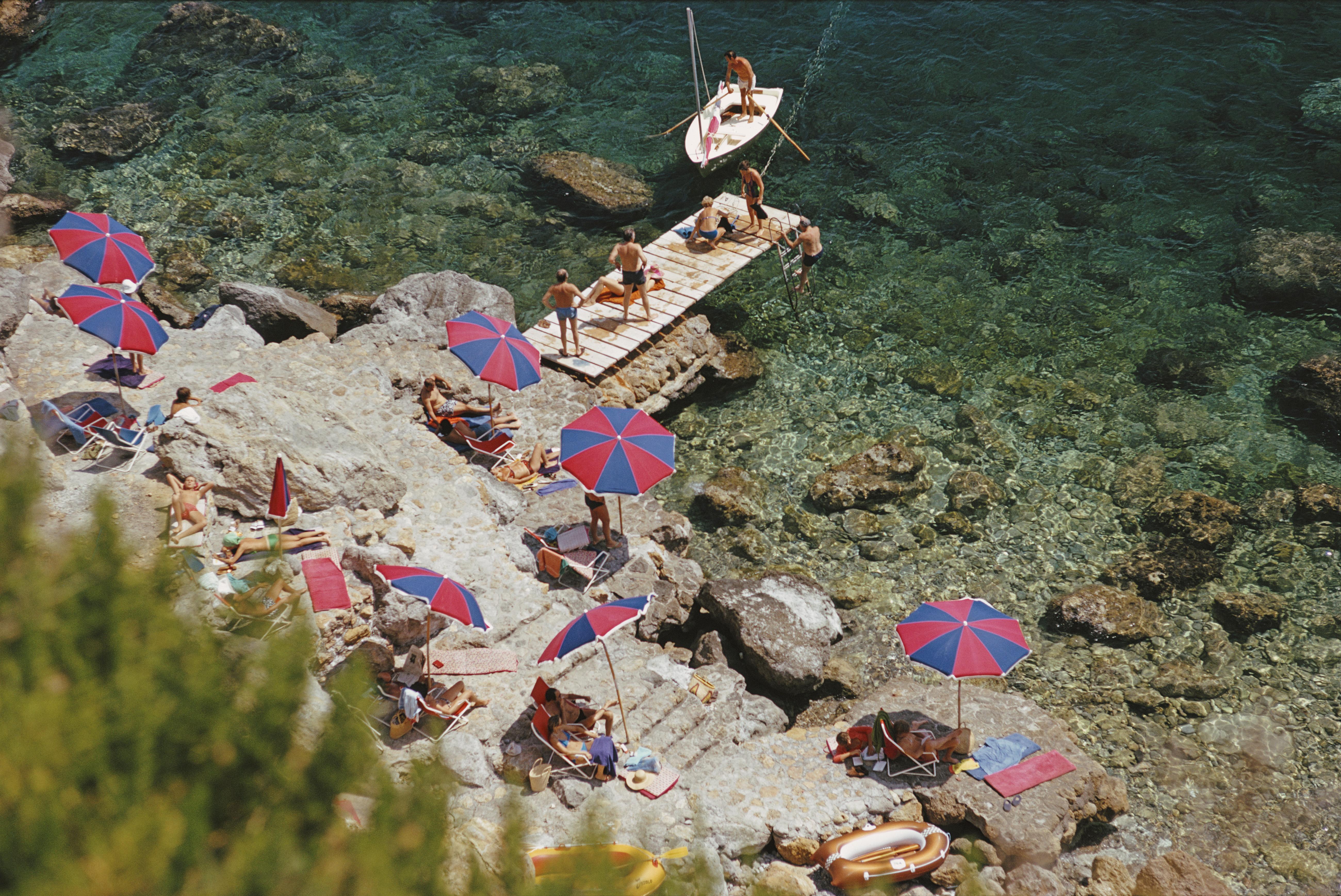 'Il Pellicano Beach' 1973 Slim Aarons Limited Estate Edition Print 

A jetty juts out from the rocky shoreline at the Hotel Il Pellicano in Porto Ercole, Tuscany, August 1973. 

Produced from the original transparency
Certificate of authenticity