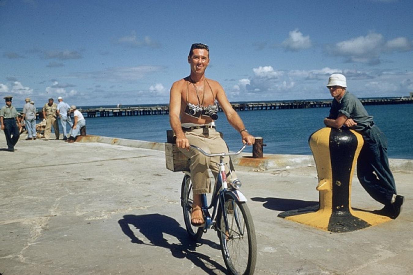 'Its A Hard Life' 1985 Slim Aarons Limited Estate Edition Print 

Photographer Slim Aarons riding a bike along the quayside with cameras slung round his neck during the filming of 'Mister Roberts' in Hawaii.

Produced from the original