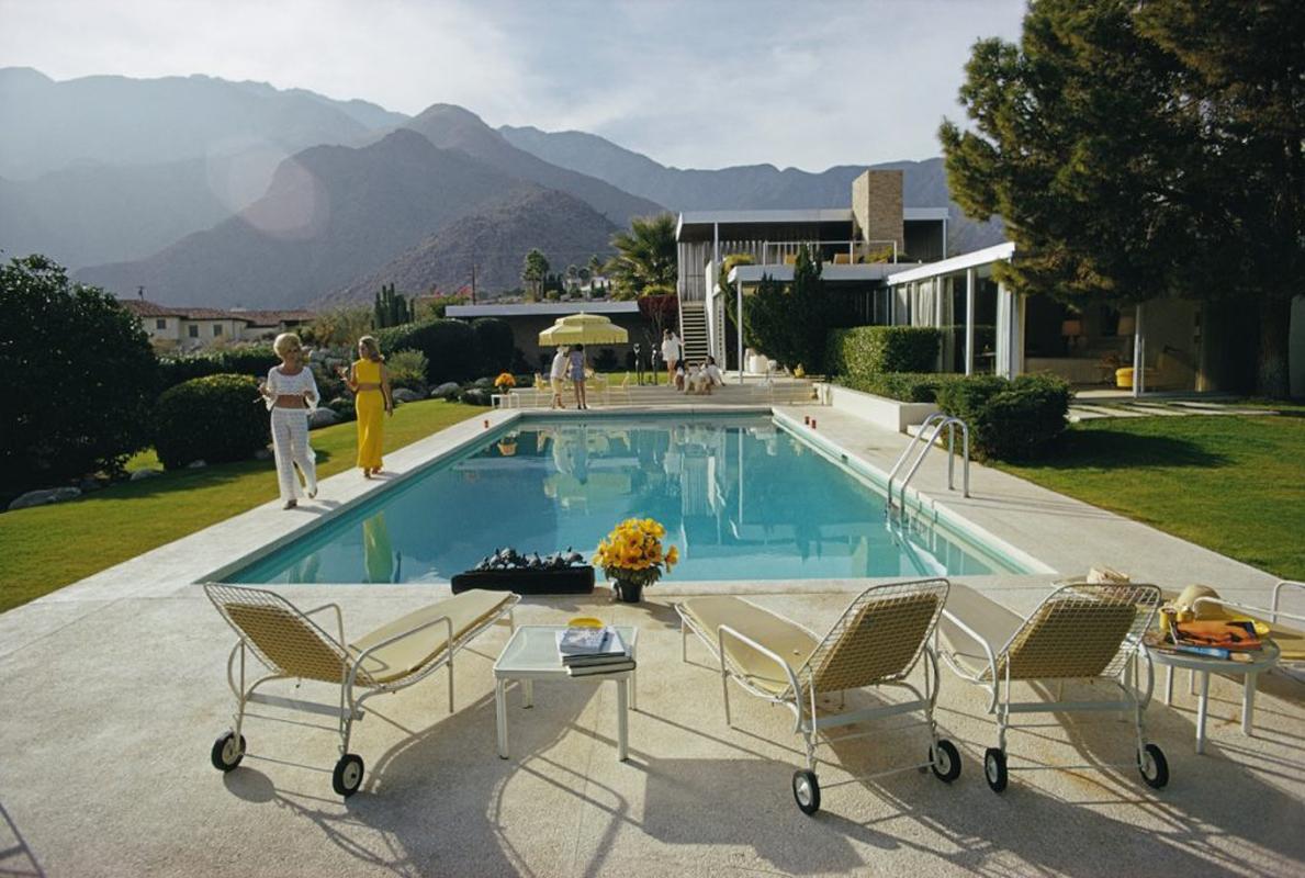 Slim Aarons Estate Limited Edition C print 30x20" inches unframed.

' Kaufmann Desert House '

Former fashion model Helen Dzo Dzo Kaptur (in white lace) and Nelda Linsk (in yellow), wife of art dealer Joseph Linsk, at the Kaufmann Desert House in