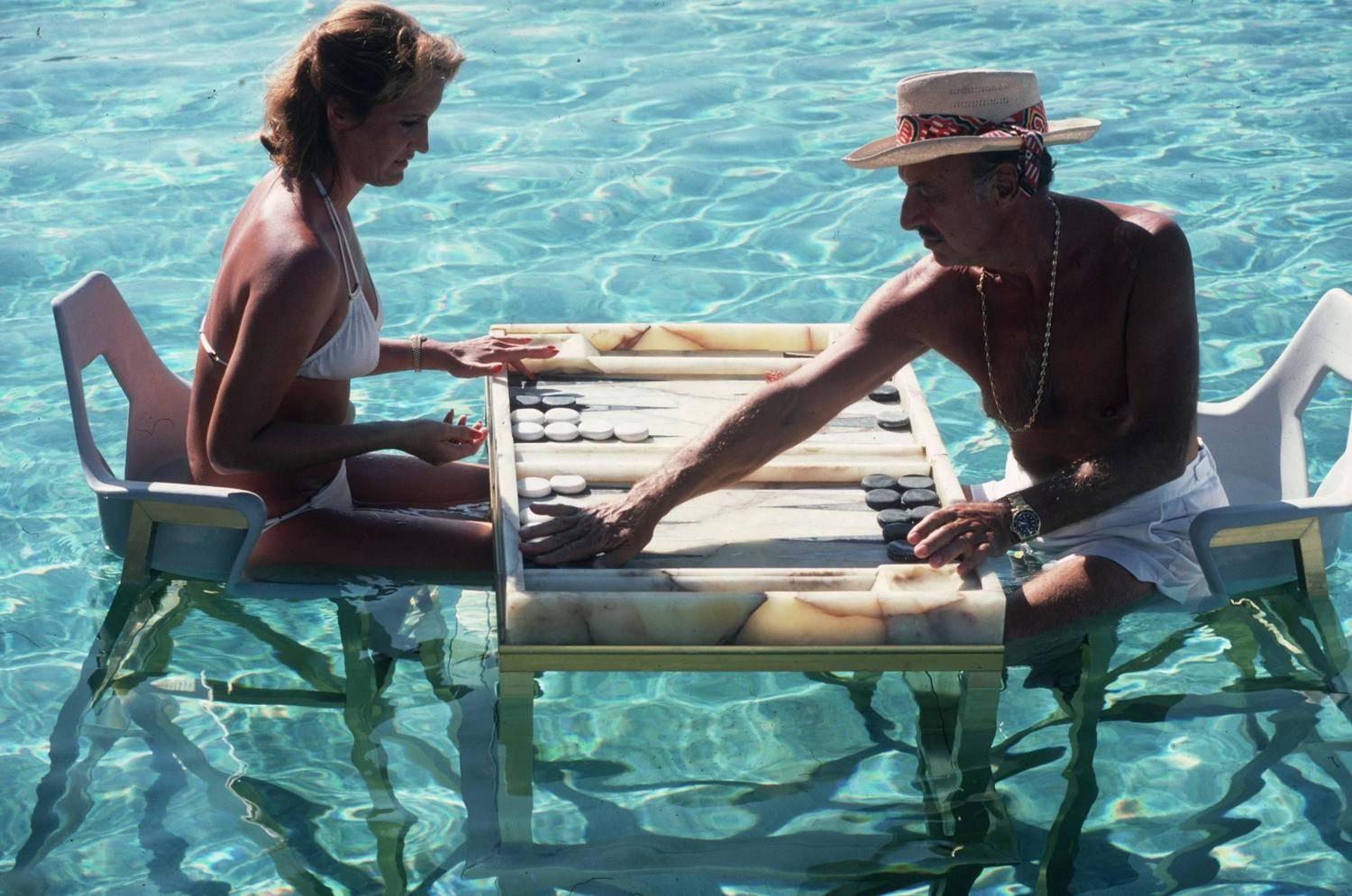 Carmen Alvarez bei einer Partie Backgammon mit Frank 'Brandy' Brandstetter in einem Schwimmbad in Acapulco, 1978.

Schlanke Aarons
Keep Your Cool (Backgammon in Acapulco)
Chromogener Lambda-Druck
Später gedruckt
Slim Aarons Estate
