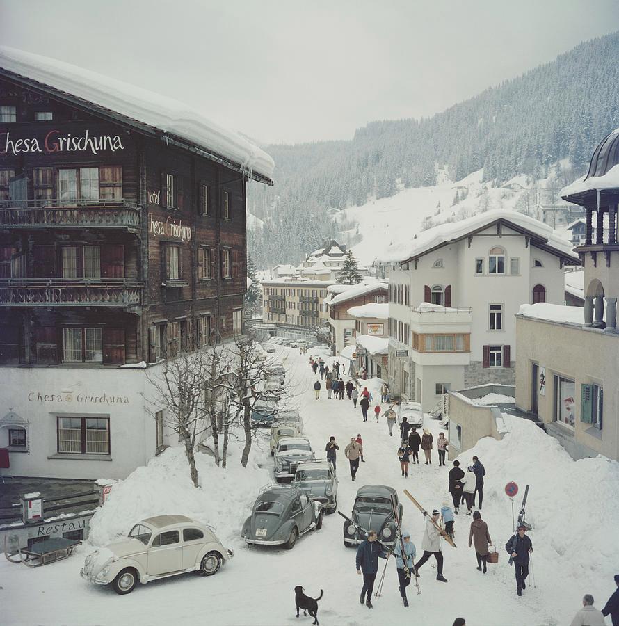 Des skieurs passent devant l'hôtel Chesa Grischuna à Klosters, en 1963.

Cette photographie fait partie de l'édition limitée à 150 exemplaires de la succession
30x30”
C-print, d'après le transparent original
Imprimé plus tard
Avec signature en