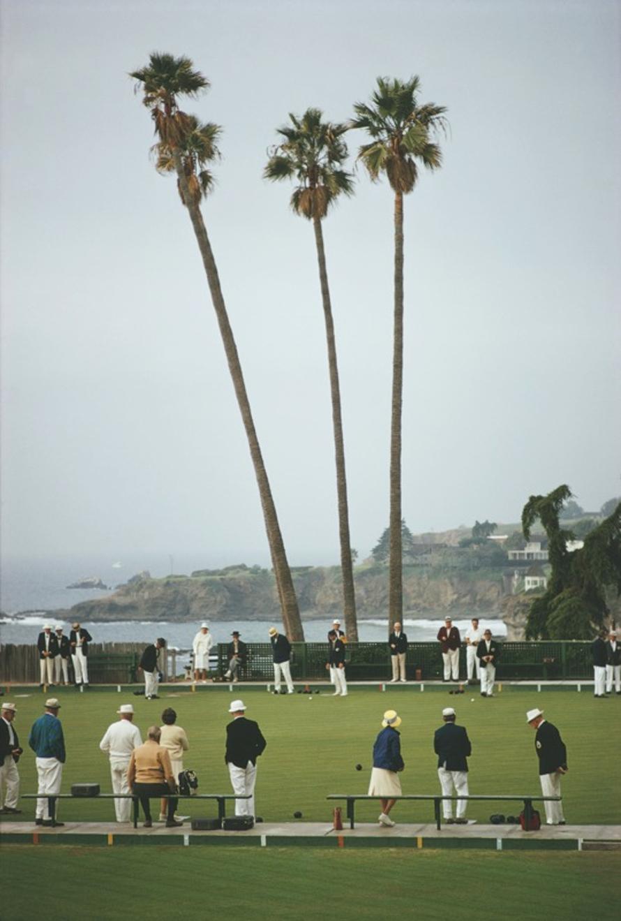 Laguna Bowls 
1970
by Slim Aarons

Slim Aarons Limited Estate Edition

 A game of bowls in progress at Laguna Beach Lawn Bowling Club in Heisler Park, southern California, circa 1970. Members and guests have to observe a strict dress