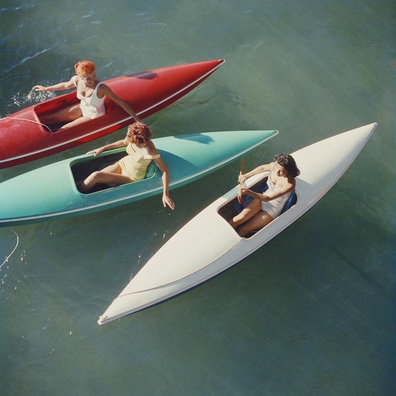 Canoe del lago Tahoe" di Slim Aarons

Giovani donne in canoa sul lato del Nevada del lago Tahoe, 1959.

Tre giovani donne sono ritratte con le loro canoe rosse, turchesi e bianche sul lago Tahoe sotto il sole. 

Questa fotografia incarna lo stile di