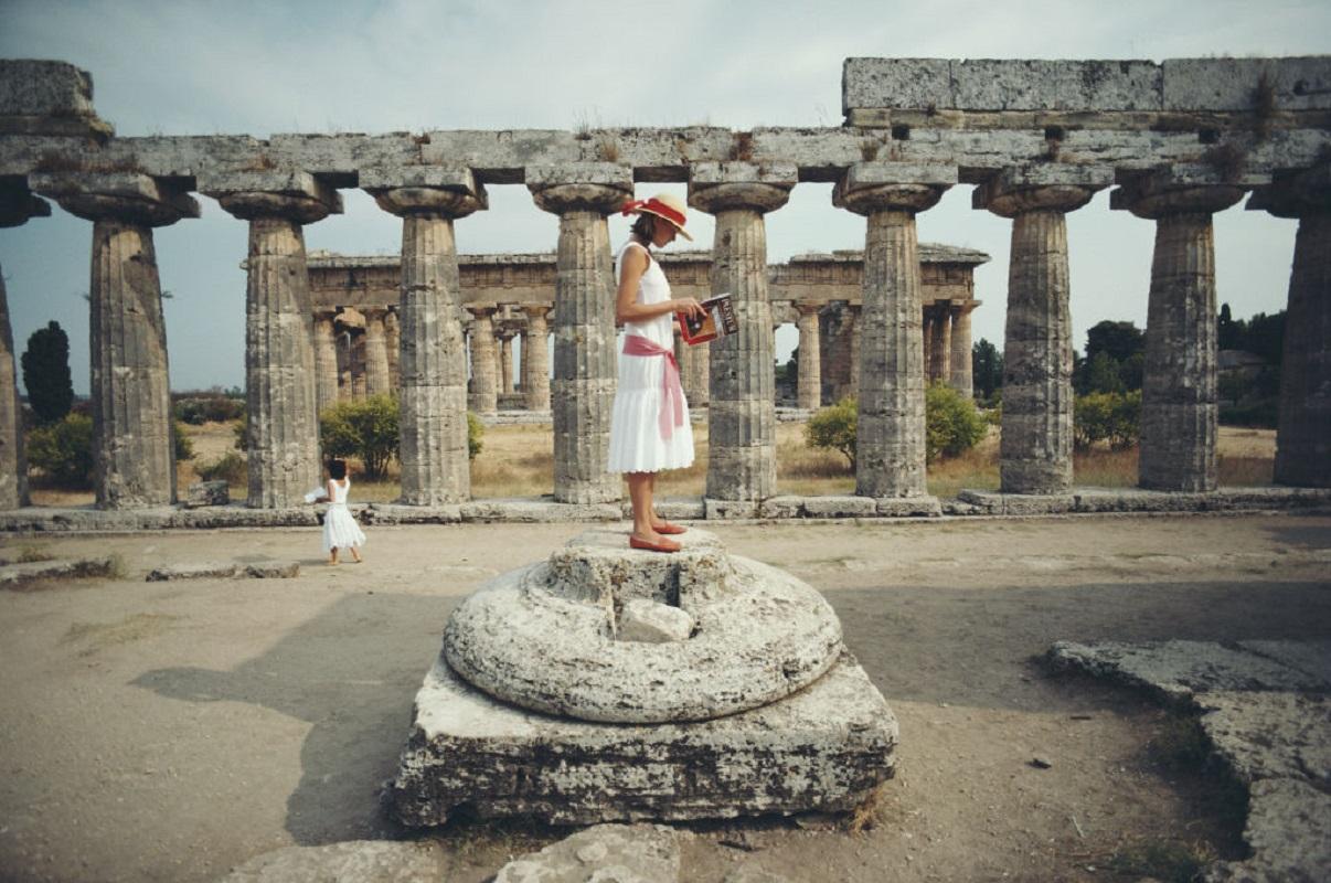 'Laura Hawk In Paestum' 1984 Slim Aarons Limited Estate Edition Print 

Laura Hawk, assistant to the photographer, poses reading a guide to Paestum while standing on the base of a broken column among the ruins of the Temple of Poseidon at Paestum,