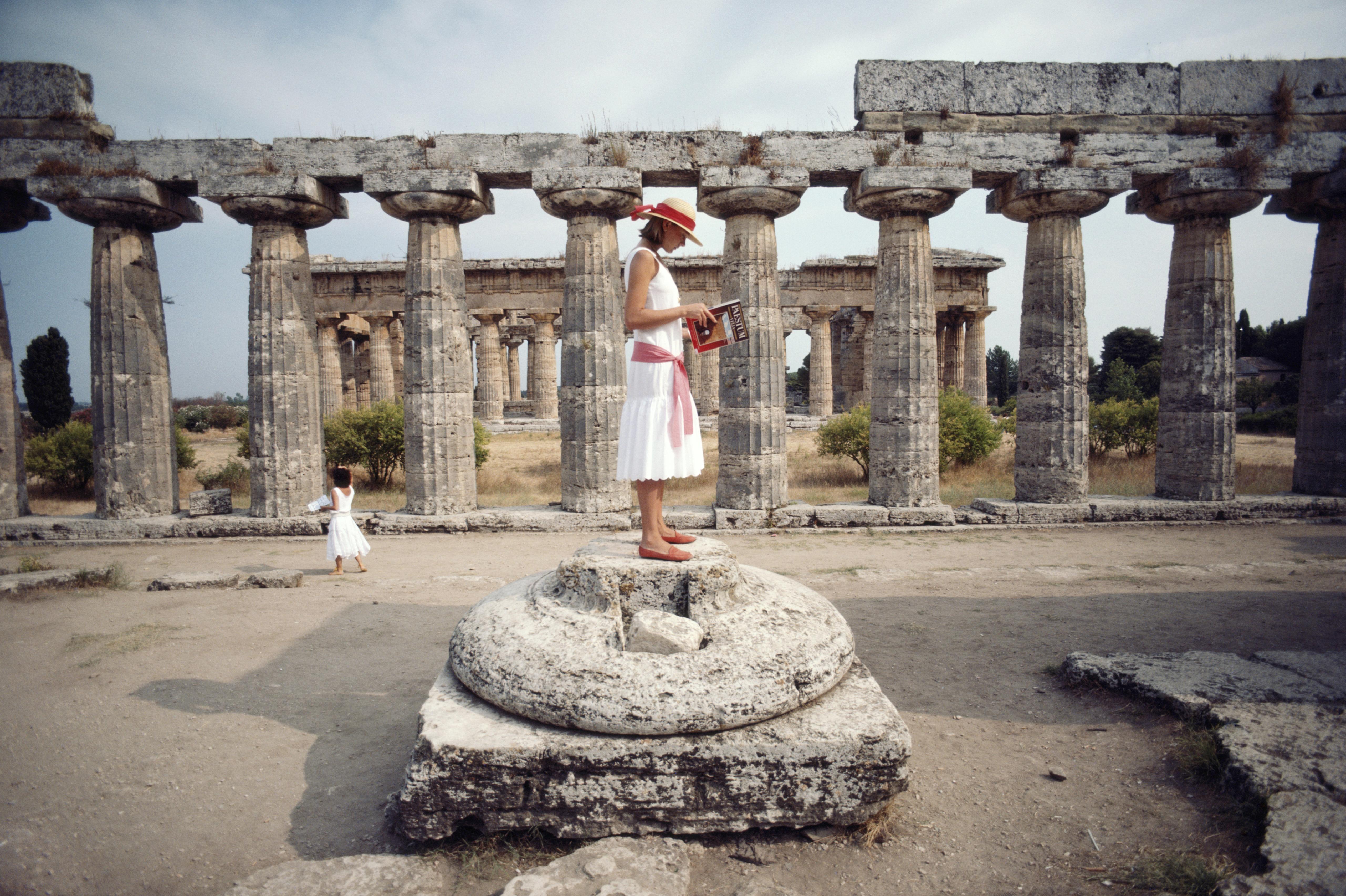 Laura Hawk, assistant to the photographer, poses reading a guide to Paestum while standing on the base of a broken column among the ruins of the Temple of Poseidon at Paestum, in the Campania region of Italy, in August 1984. 

C-type print from the