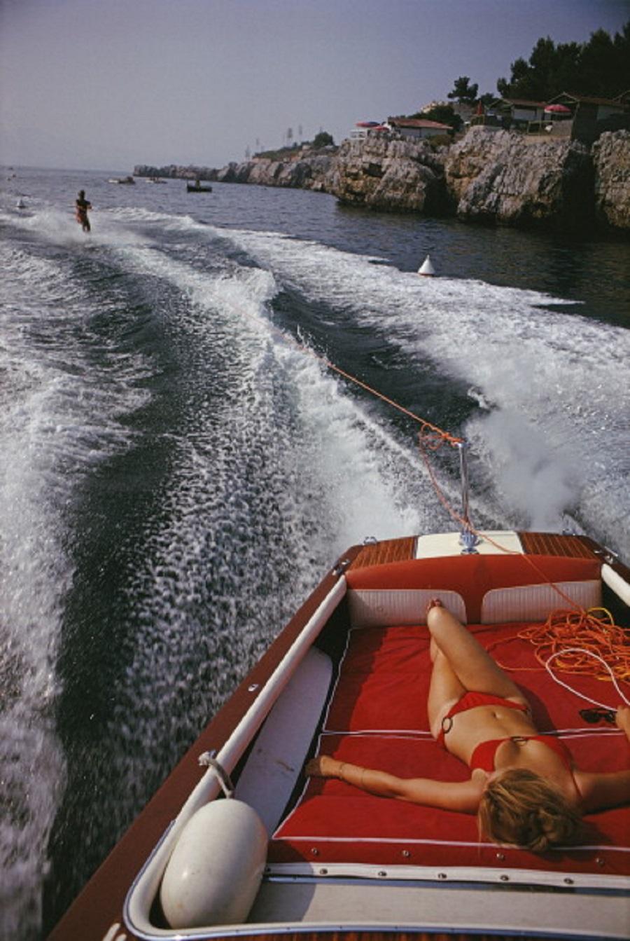 'Leisure In Antibes' 1969 Slim Aarons Limited Estate Edition Print 

A woman sunbathing in a motorboat as it tows a waterskiier, in the sea off the Hotel du Cap-Eden-Roc in Antibes on the French Riviera, August 1969. 

Produced from the original