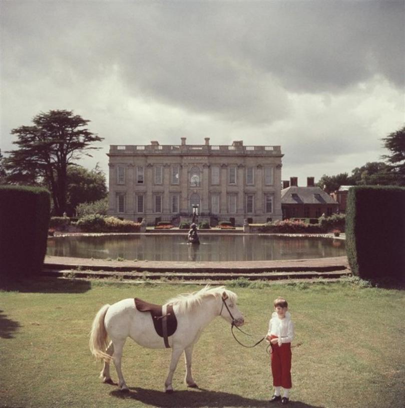 Lord Of All I Survey 
1959
by Slim Aarons

Slim Aarons Limited Estate Edition

The youngest peer in England, seven year old Thomas Alexander Fermor-Hesketh, 3rd Baron and 10th Baronet Hesketh with his pony ‘Blossom’ by the lake in the magnificent