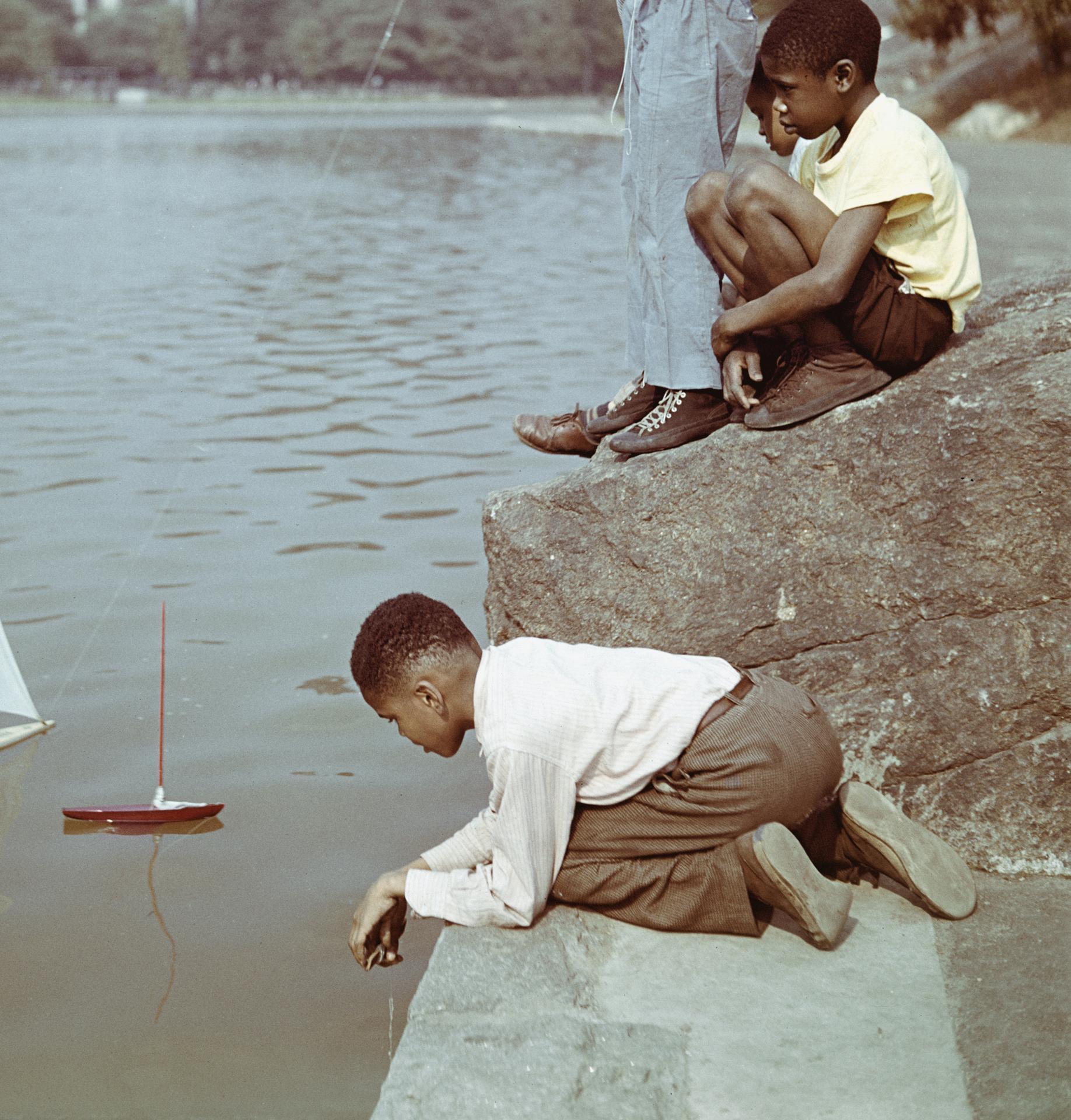 This late 1940s urban portrait photograph, captured by society photographer Slim Aarons, features a group of young boys sailing model boats at Harlem Meer, Central Park, New York City, New York.

This is an estate stamped and hand numbered edition