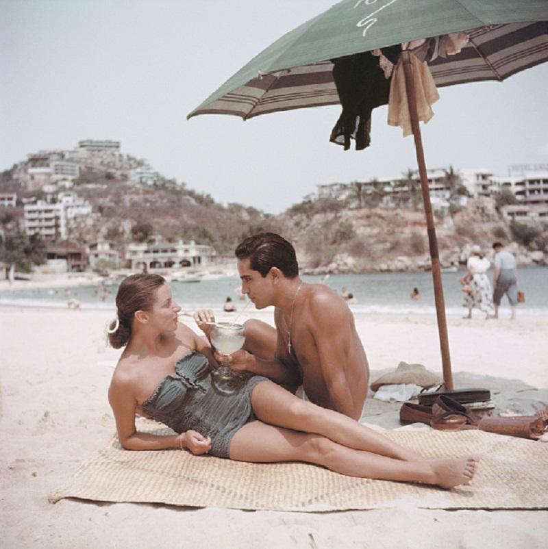 'Model Friend' 1952 Slim Aarons Limited Estate Edition Print 

1952: New York model, Jean Adams and friend share a drink on the beach at Acapulco. 

Produced from the original transparency
Certificate of authenticity supplied 
Archive stamped

Paper