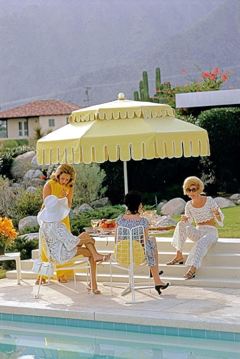 palm Springs Life' 1970 Slim Aarons Limitierte Nachlassausgabe Druck 

Nelda Linsk (links, in gelb), Ehefrau des Kunsthändlers Joseph Linsk, mit Gästen am Pool des Wüstenhauses der Linsks in Palm Springs, Januar 1970. Ganz links mit weißem Sonnenhut