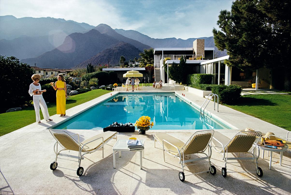 Palm Springs Pool 
1970
by Slim Aarons

Slim Aarons Limited Estate Edition

Former fashion model Helen Dzo Dzo Kaptur (in white lace) and Nelda Linsk (in yellow), wife of art dealer Joseph Linsk, at the Kaufmann Desert House in Palm Springs,
