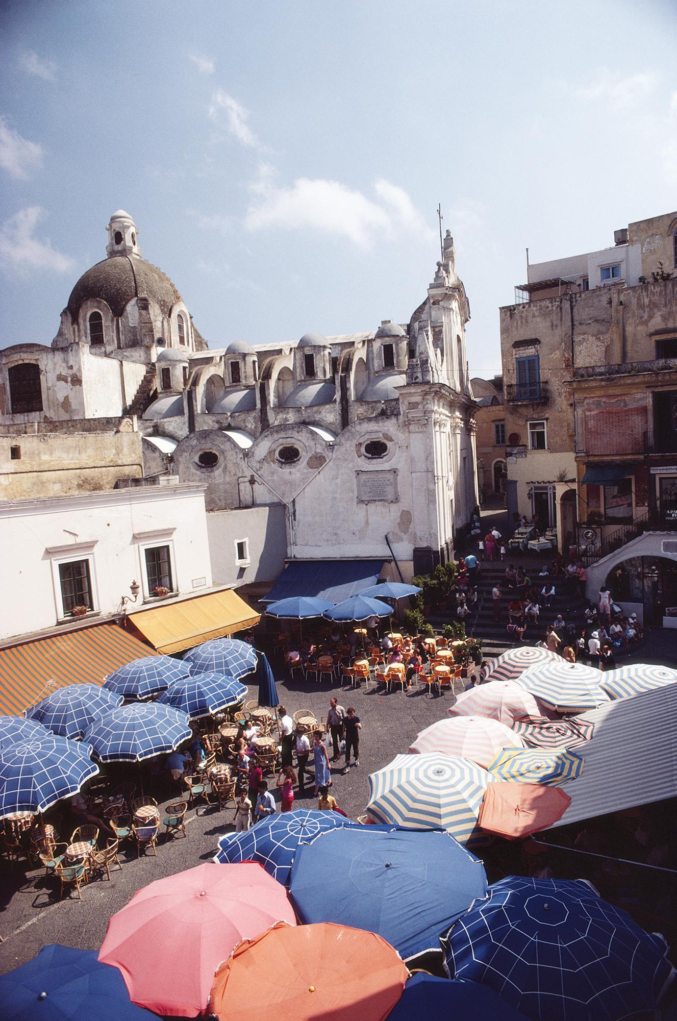 This early-1980s photograph, taken by society photographer Slim Aarons, features an aerial view of a parasols shading customers at cafes and restaurants in the Piazza Umberto, on the island of Capri, Italy.

This is an estate-stamped and
