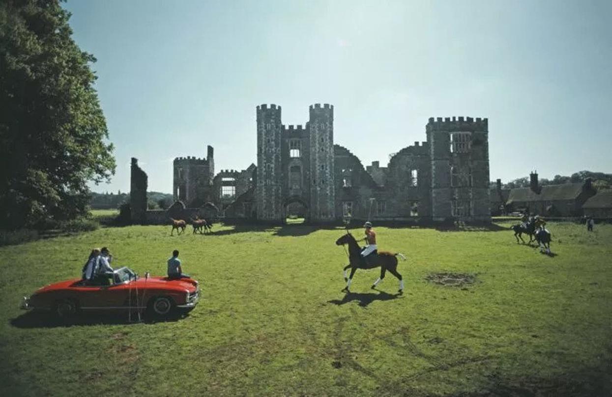 Polo At Cowdray Park 
1985
by Slim Aarons

Slim Aarons Limited Estate Edition

Three people sitting on a red Mercedes convertible watch polo players in action at Cowdray Park, West Sussex, August 1985. In the background are the ruins of Cowdray