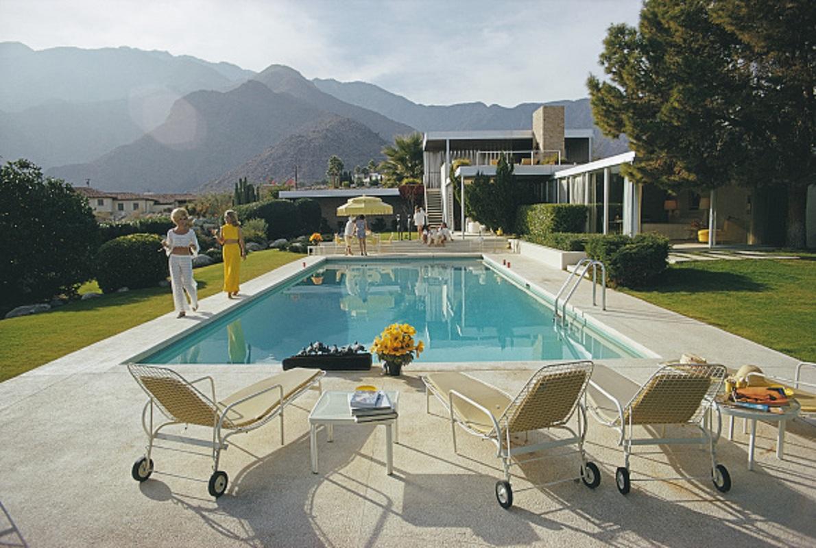 'Poolside Catwalk' 1970 Slim Aarons Limited Estate Edition Print 

Former fashion model Helen Dzo Dzo Kaptur (in white lace) and Nelda Linsk (in yellow), wife of art dealer Joseph Linsk, at the Kaufmann Desert House in Palm Springs, California,
