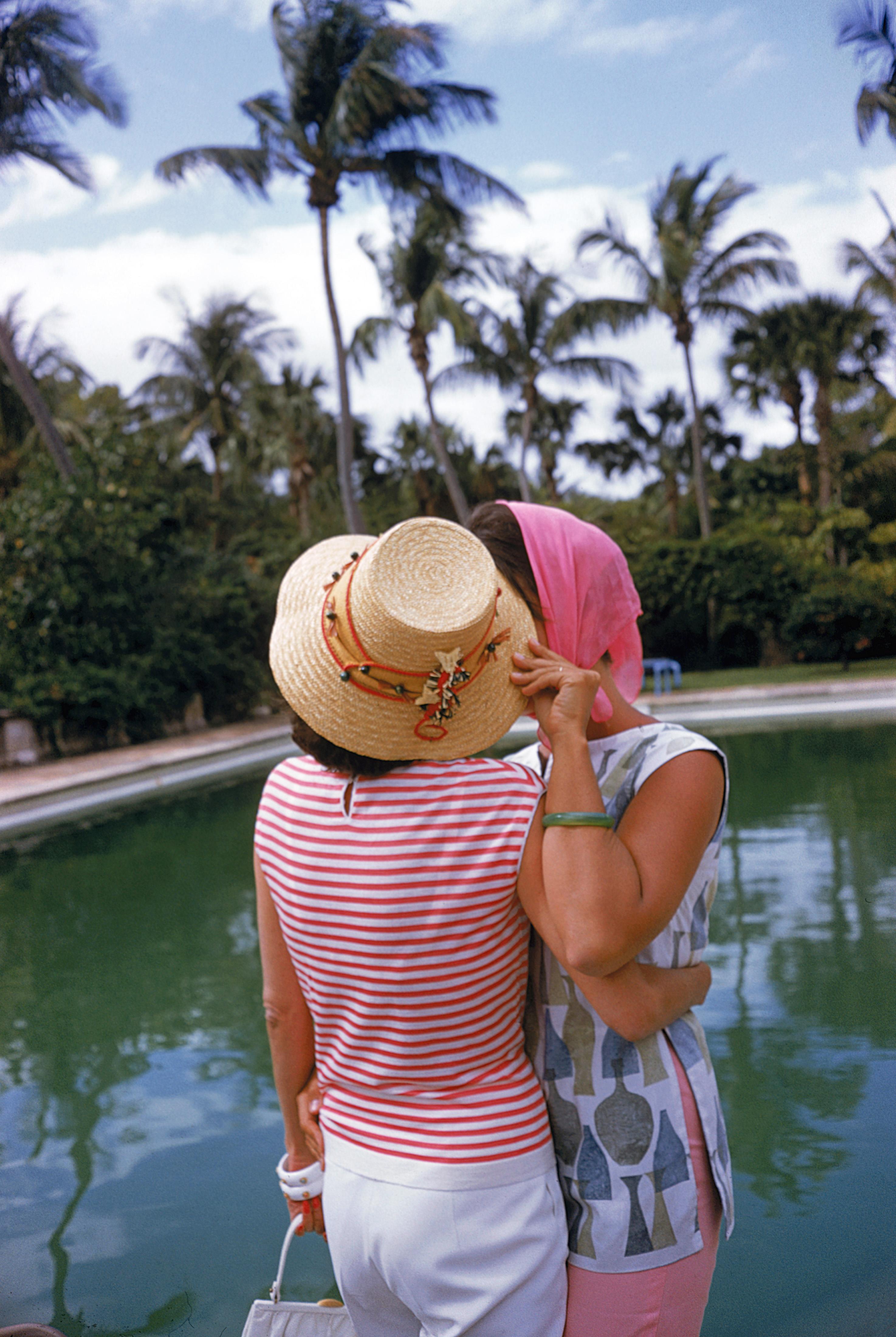 Flo Smith (left) and Lily Pulitzer share a secret at a pool party, Palm Beach, Florida, April 1961.

Description and alt text: In this classic image of midcentury poolside glamour, two suntanned white women share a moment by the sparkling blue and