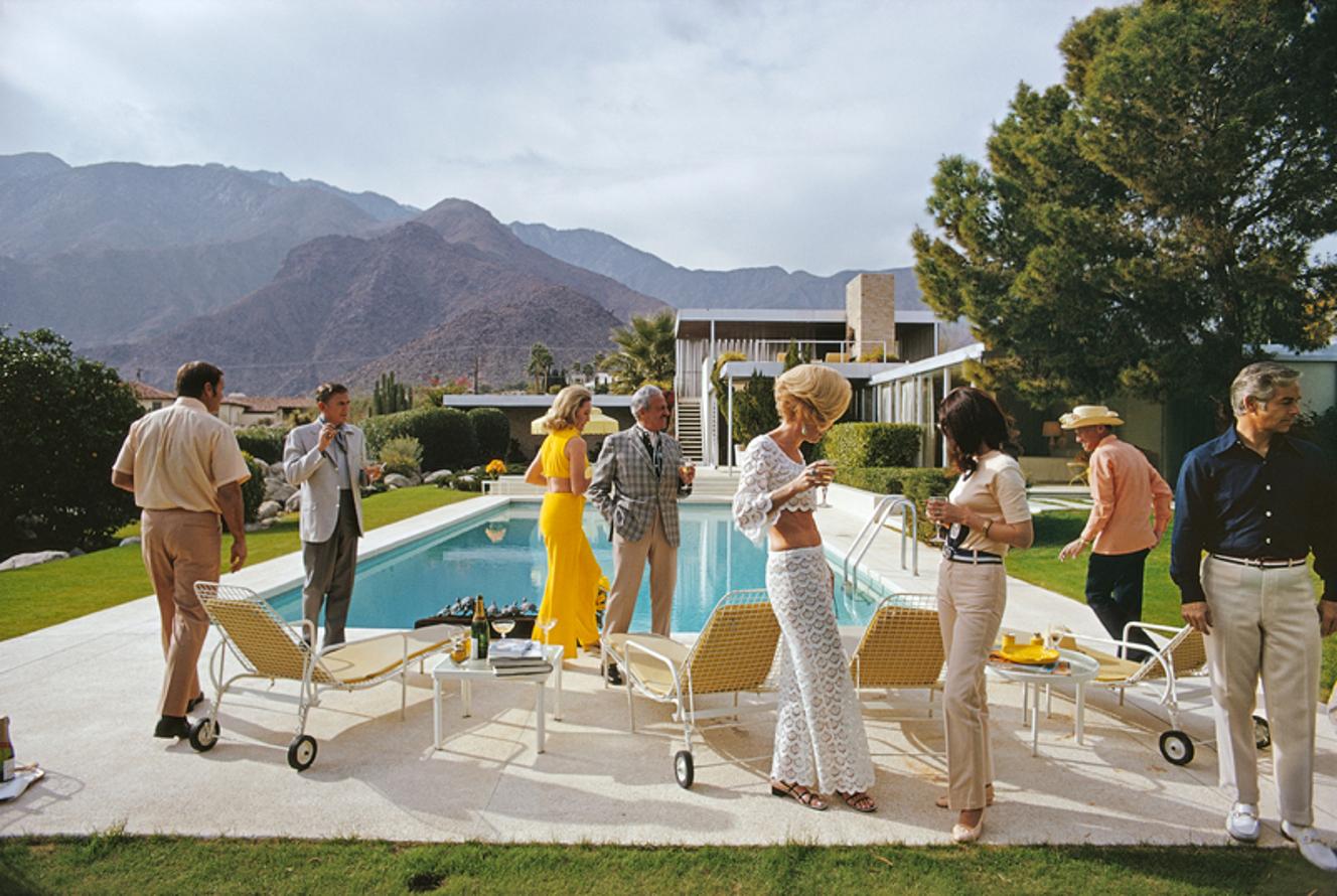 Poolside Style 
1970
by Slim Aarons

Slim Aarons Limited Estate Edition

Former fashion model Helen Dzo Dzo Kaptur (in white lace), Nelda Linsk (in yellow), wife of art dealer Joseph Linsk, and other guests at the Kaufmann Desert House in Palm