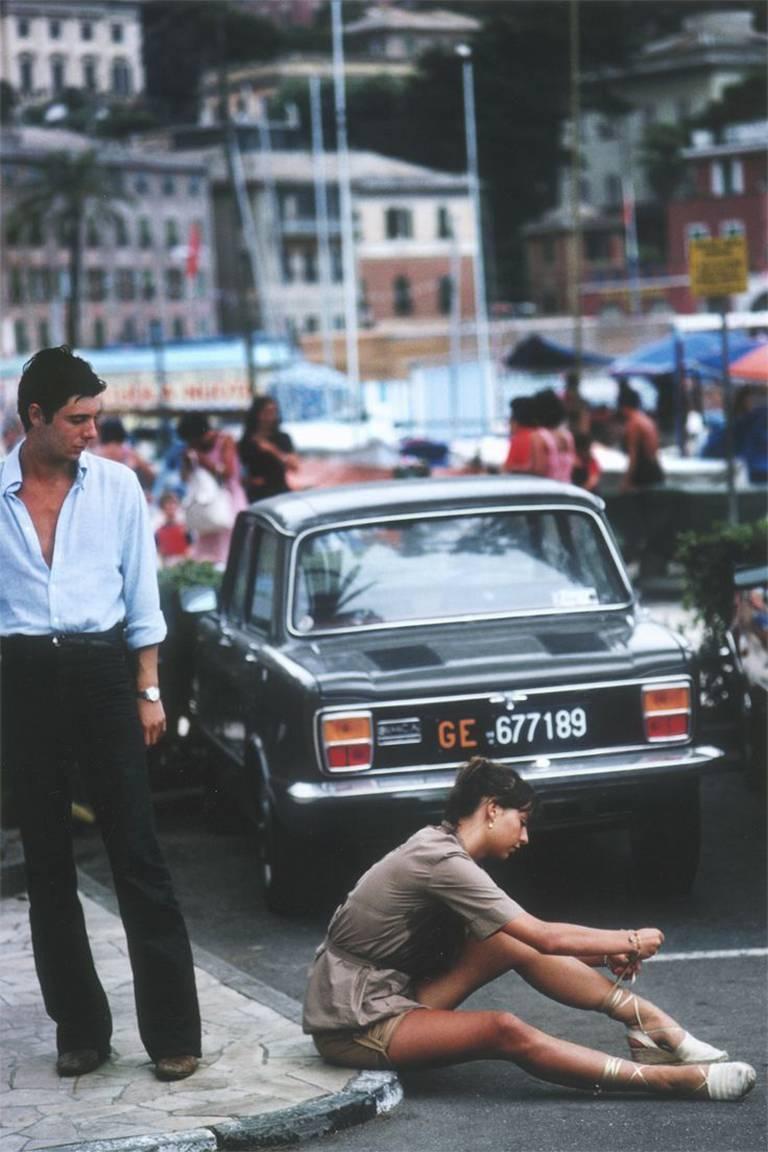Ein Mann bleibt stehen, um einer jungen Frau beim Binden ihrer Sandalen auf dem Bürgersteig im Yachthafen von Portofino zuzusehen, August 1977.

Nachlassgestempelte und handnummerierte Auflage von 150 Stück mit Echtheitszertifikat des Nachlasses.