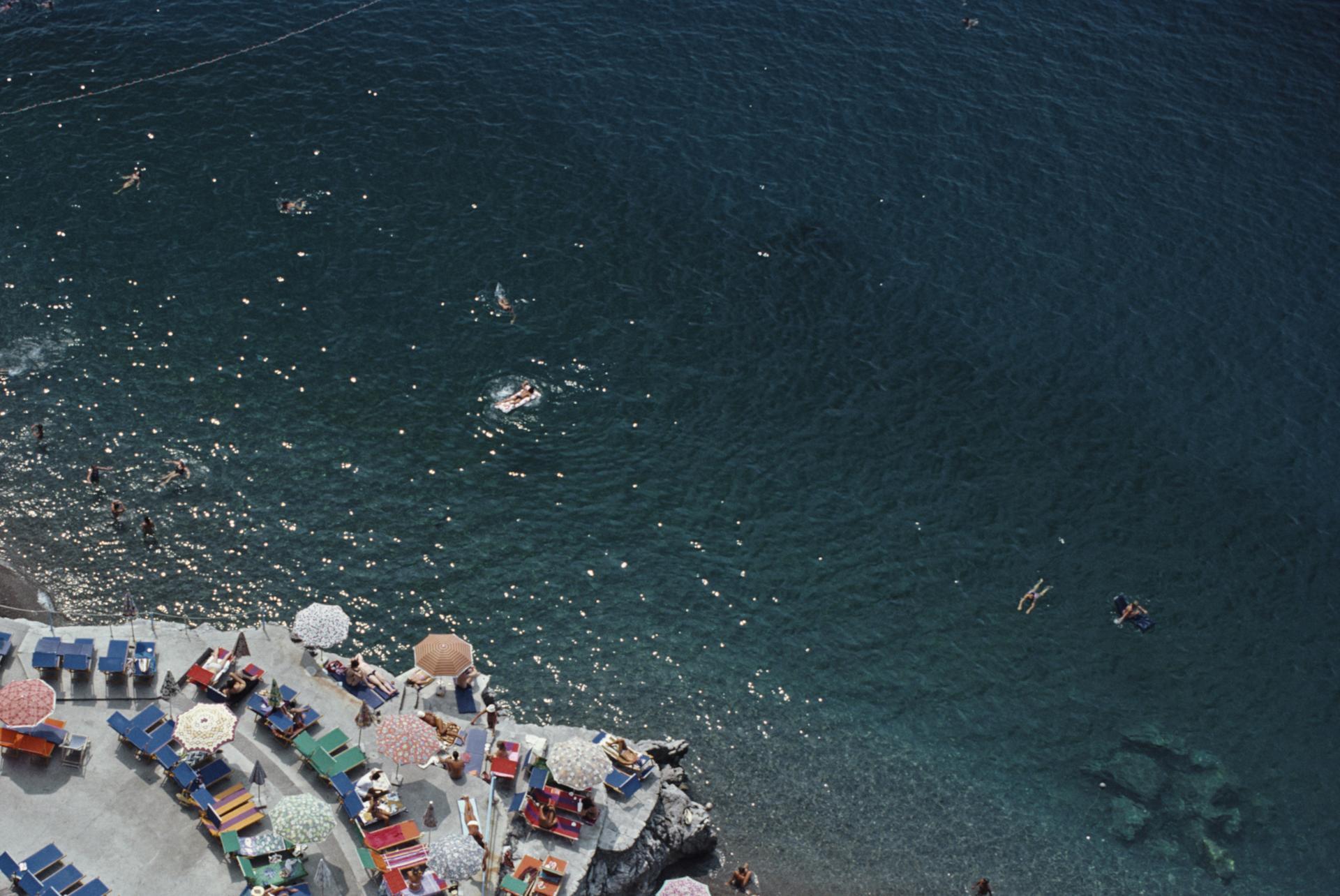 Vue surélevée de personnes prenant le soleil et de parasols sur la plage de La Scogliera à Positano, Italie, 1979. 

Slim Aarons Estate Edition, certificat d'authenticité inclus.
Numéroté et tamponné par la succession Slim Aarons
Le collectionneur