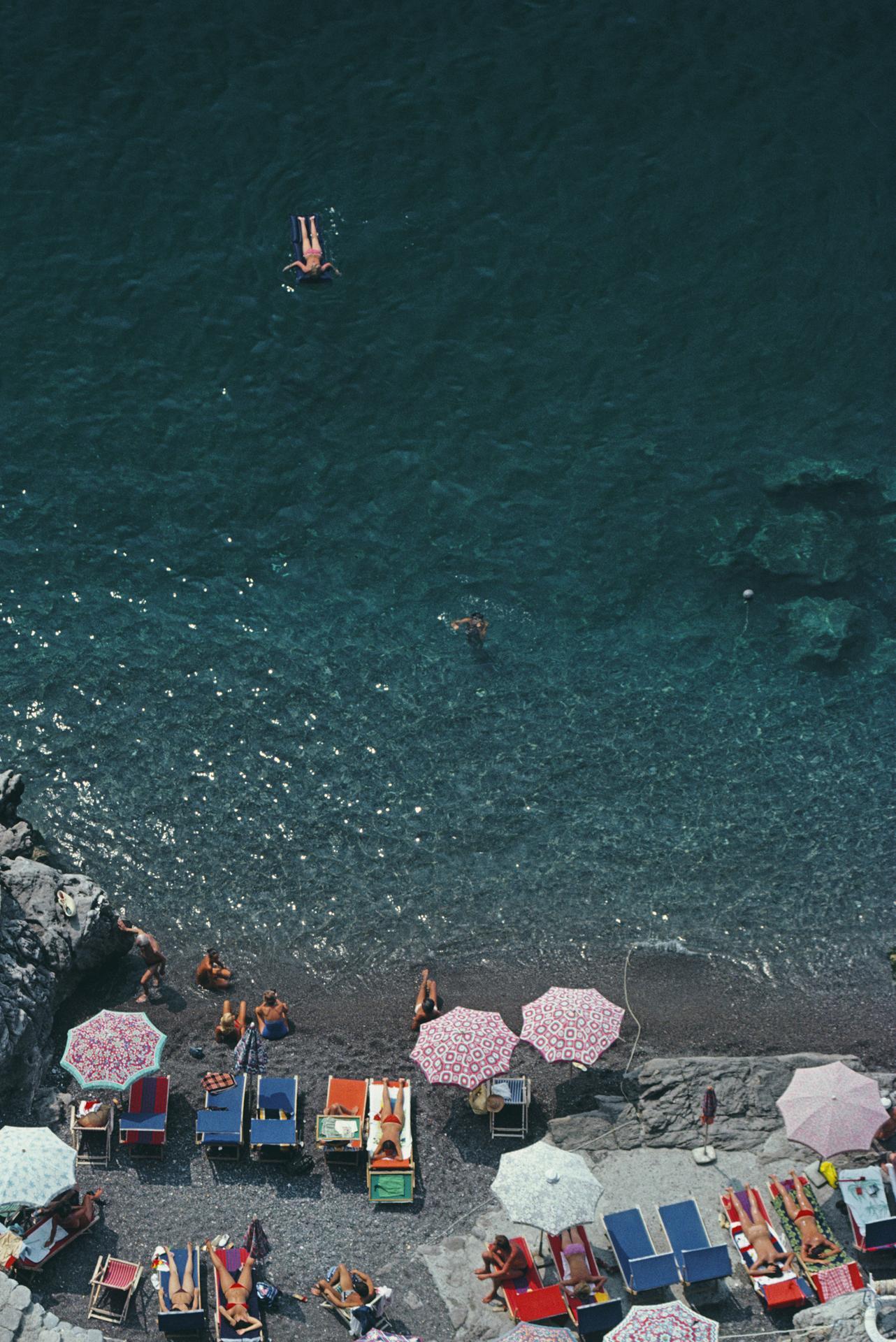 Vue surélevée de personnes prenant le soleil et de parasols sur la plage de La Scogliera à Positano, Italie, 1979. 

Slim Aarons Estate Edition, certificat d'authenticité inclus.
Numéroté et tamponné par la succession Slim Aarons
Le collectionneur