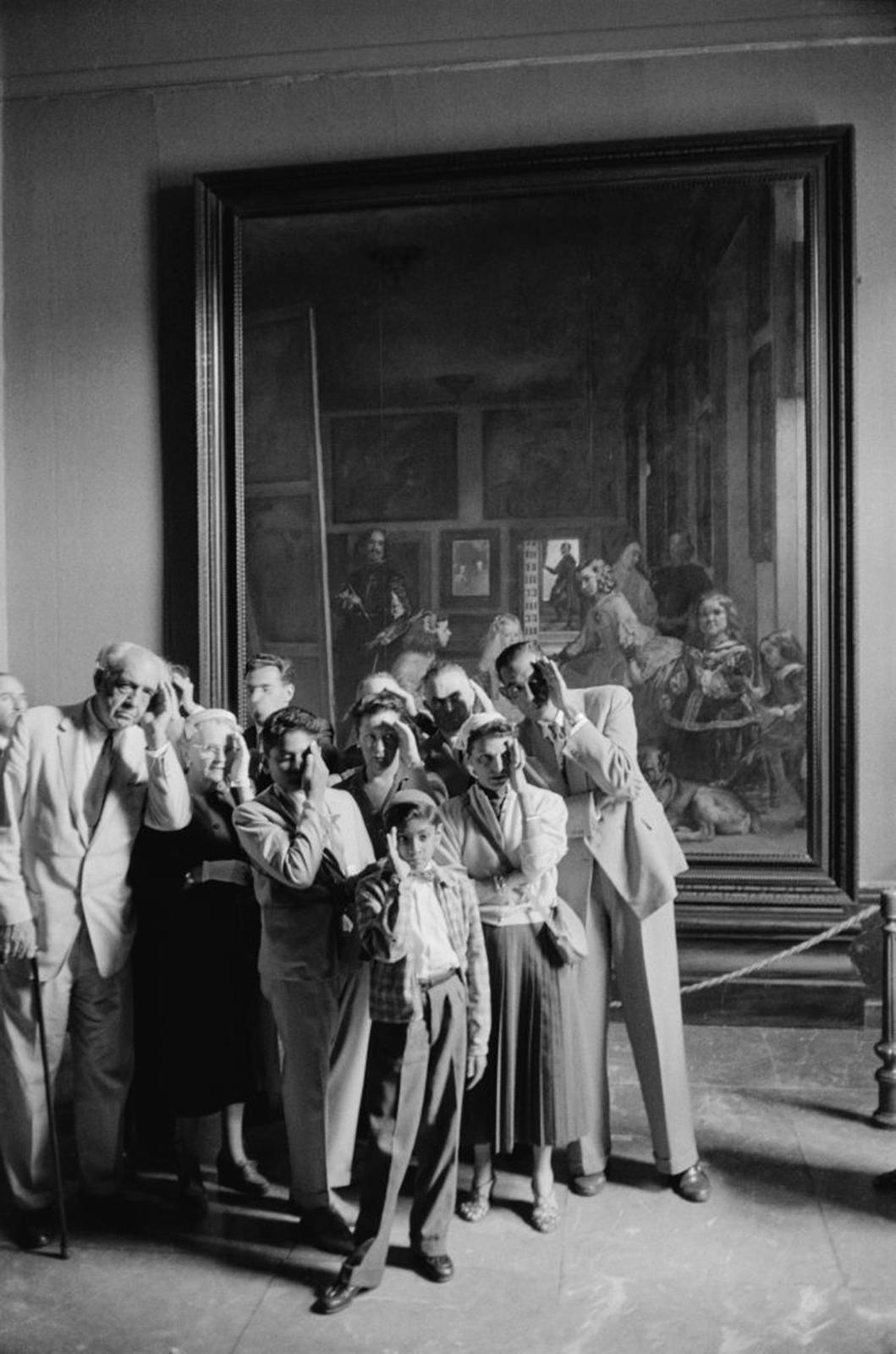 This mid-1950s portrait photograph, captured by society photographer Slim Aarons, features visitors at the The Prado Museum (Museo Nacional del Prado) viewing Diego Velázquez's masterpiece 'Las Meninas' via a mirror hung across the room, Madrid,