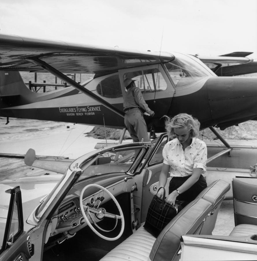 Private Transport 
1954
by Slim Aarons

Slim Aarons Limited Estate Edition

Gladys ‘Patsy’ Bartlett (1928 – 2011, née Pulitzer, later Pulitzer Preston) rummaging in her bag on the seat of an open car, 1954. The car is parked by a plane belonging to