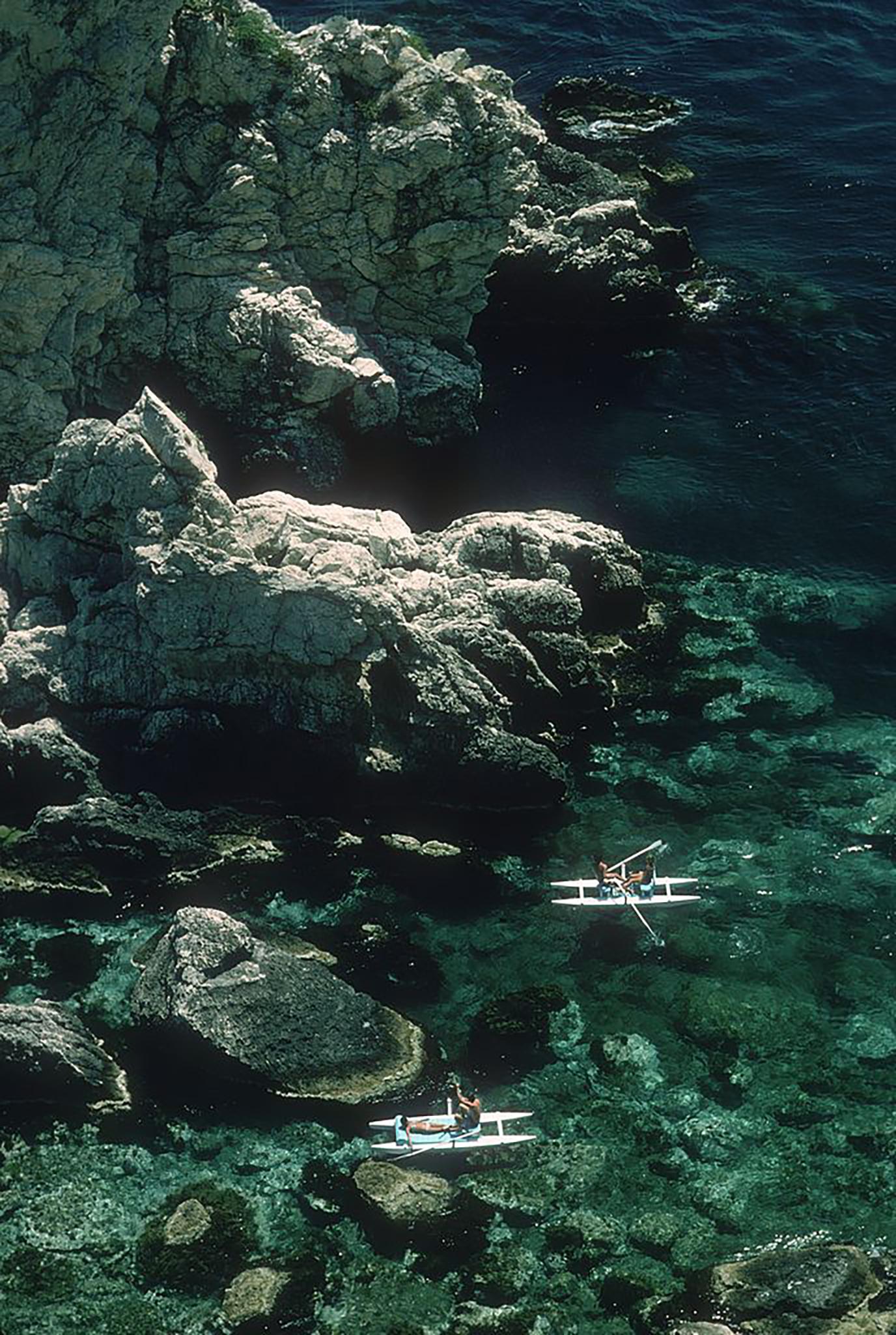 Color Photograph de Slim Aarons - Remando frente a Sicilia, Edición Inmobiliaria (Taormina, Italia: paisaje marino rocoso de color turquesa)