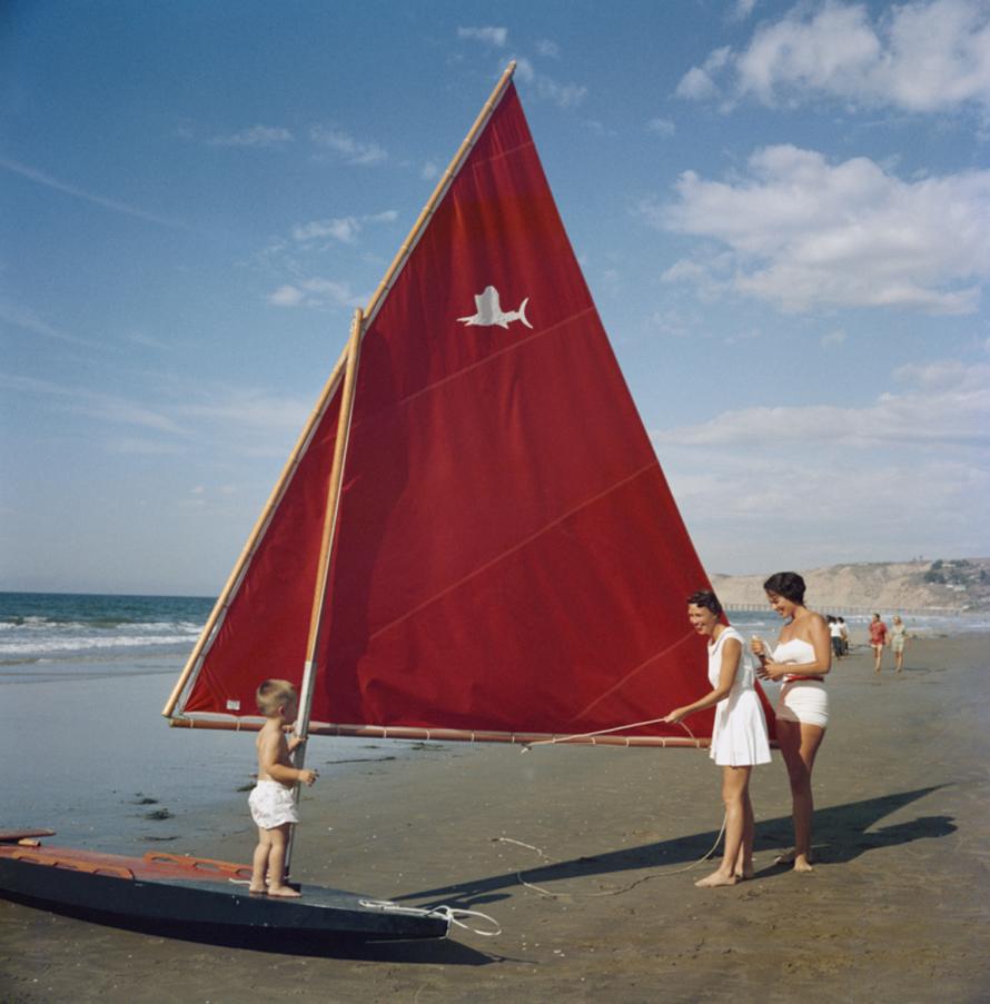 Sailboat In San Diego 
1960
by Slim Aarons

Slim Aarons Limited Estate Edition

Mrs Cuddihy Perry, her son, and Mrs George H. Gentry with a sailboat on a beach in San Diego California, 1960. 

unframed
c type print
printed 2023
16 × 16 inches -