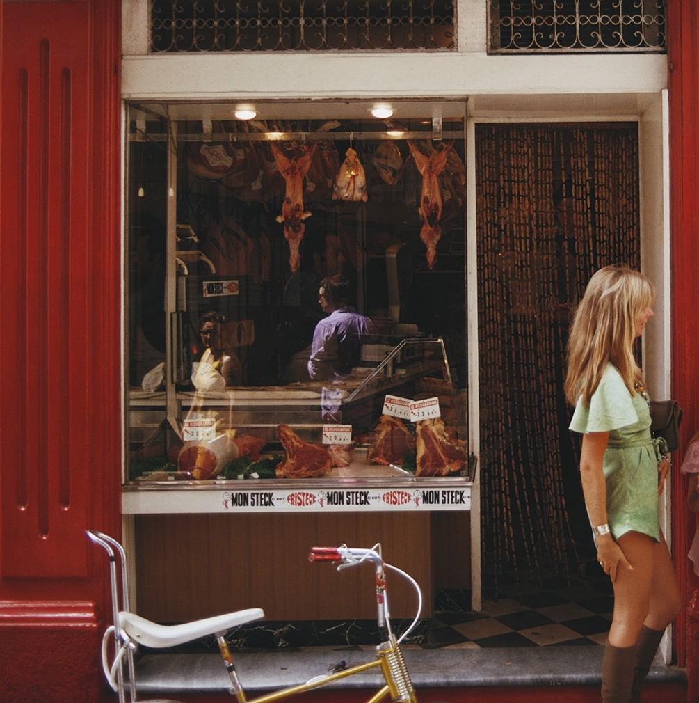 Boucherie di Saint Tropez, agosto 1971 - Donne in pantaloncini colorati fuori dal Butching - Color Photograph Marrone di Slim Aarons