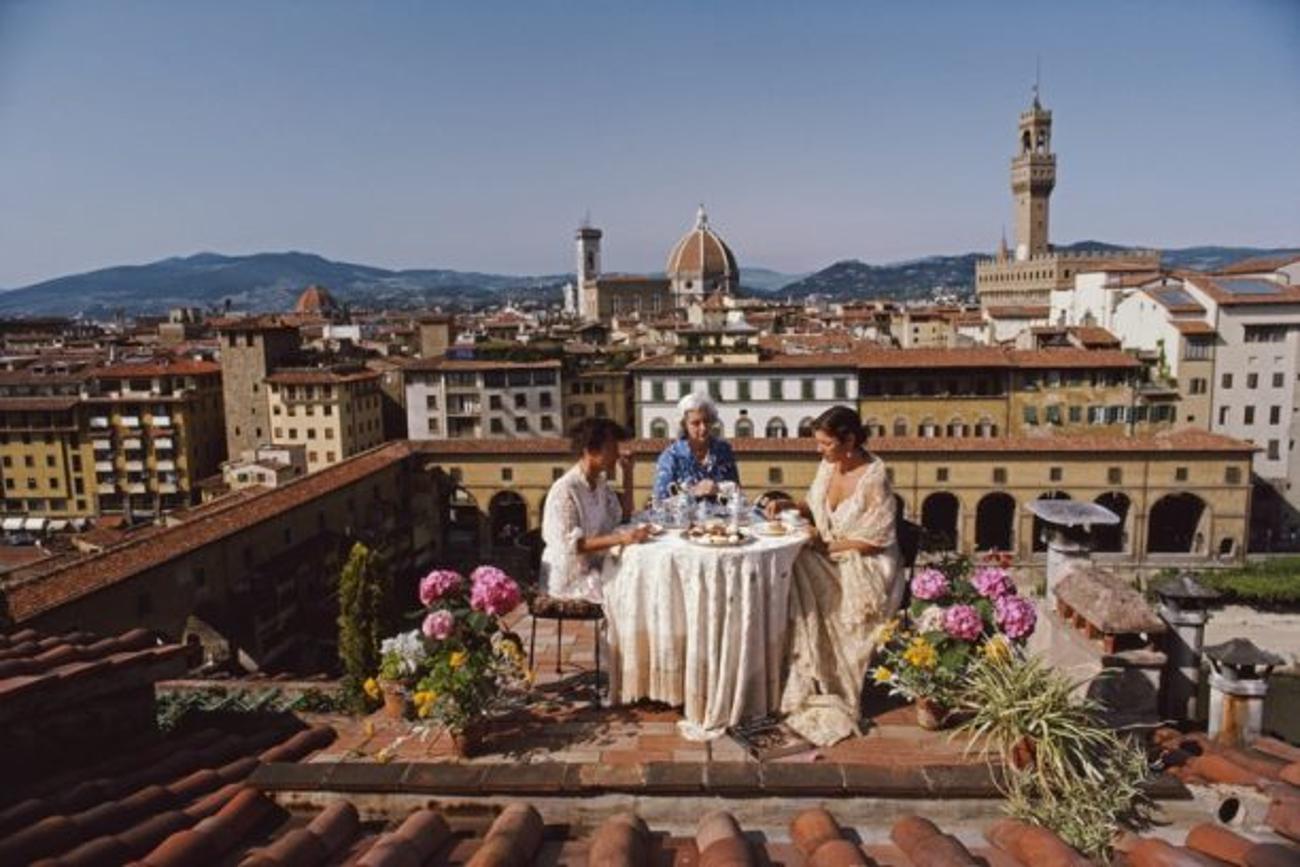Santa And Serena Antonelli 
1983
by Slim Aarons

Slim Aarons Limited Estate Edition

Santa and Serena Antonelli and a guest dining al fresco on the terrace of their home above Via Giucciardini, in Florence, Italy, 1983. Rising beyond are the dome of