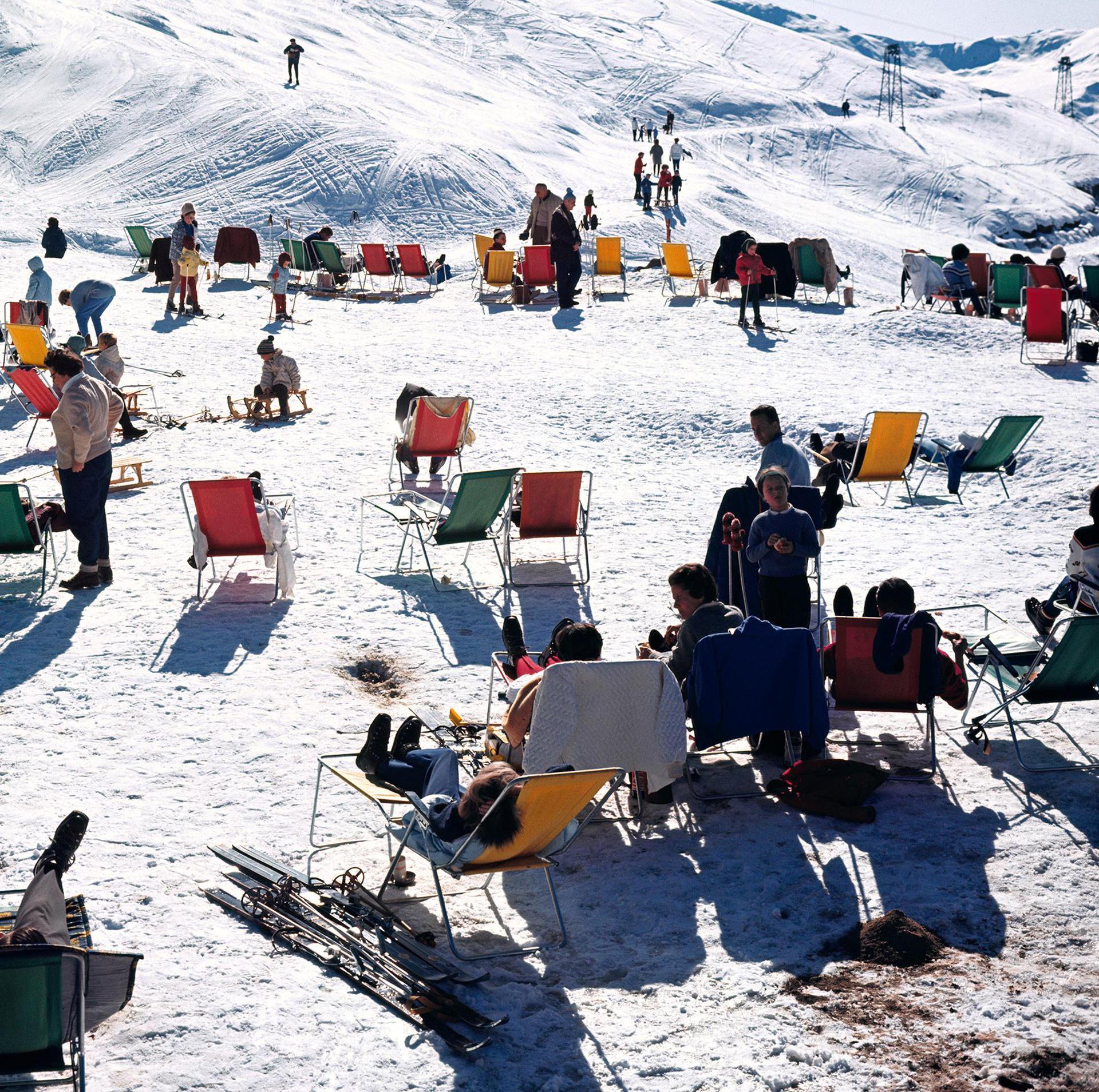 Dieses Landschaftsfoto des Society-Fotografen Slim Aarons aus den späten 1960er Jahren zeigt Skifahrer, die sich in Liegestühlen auf den Pisten von Verbier in der Schweiz entspannen. 1964.

Dies ist eine nachlassgestempelte und handnummerierte