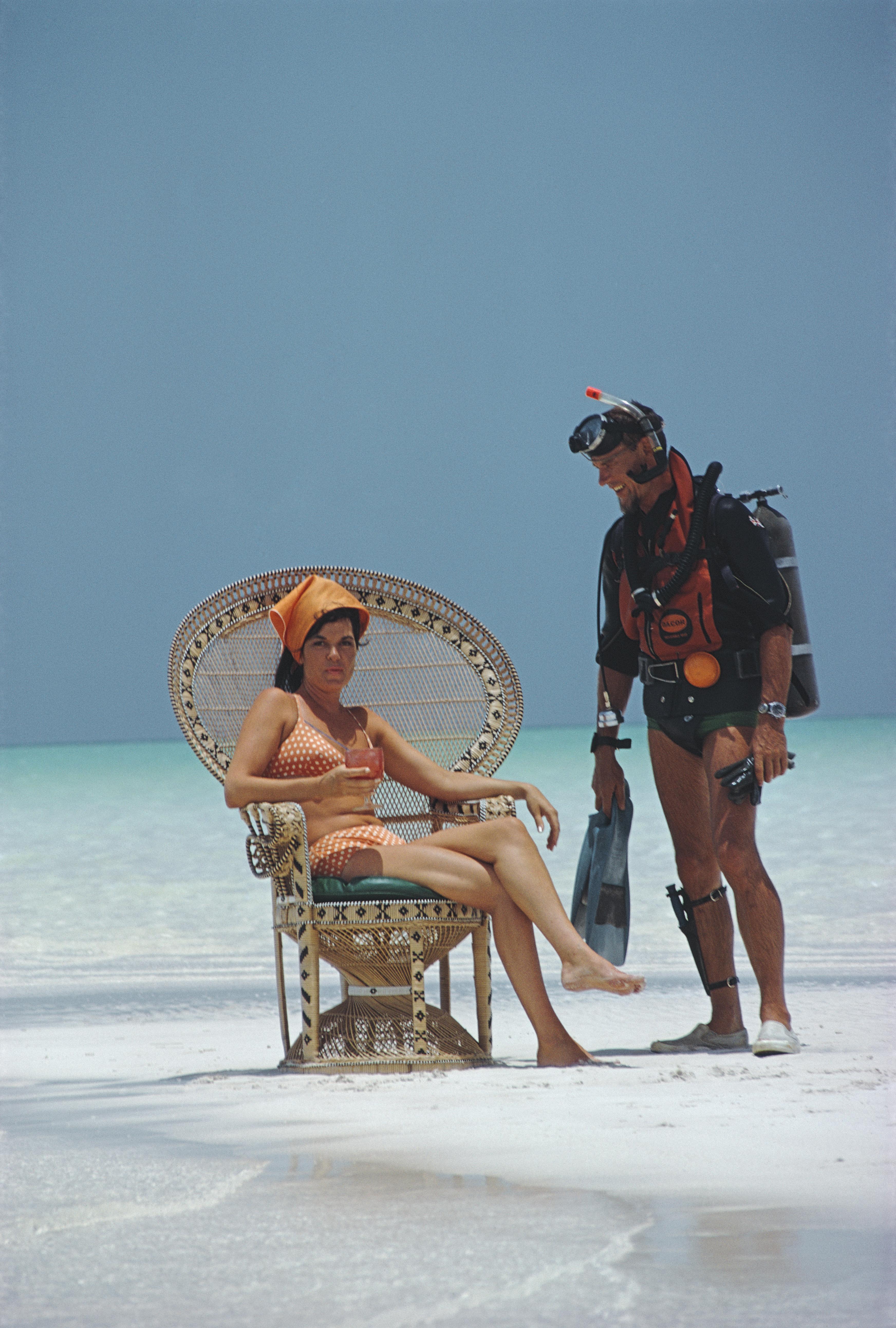 Un homme portant un équipement de plongée discute avec une jeune fille dans un fauteuil en osier sur la plage, Bahamas, 1967, Impression ultérieure

Slim Aarons
Une discussion amicale
Bahamas
Tirage chromogène Lambda 
Slim Aarons Estate
