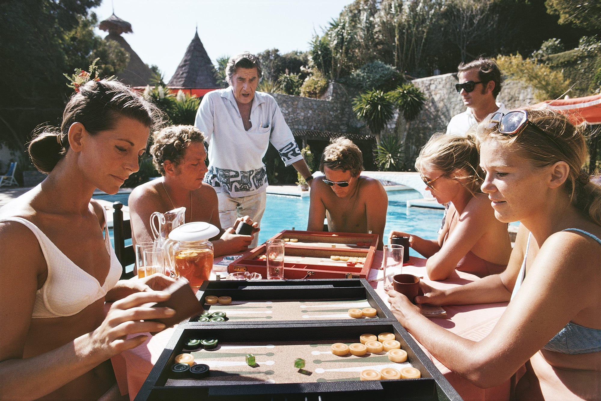 A group of people playing backgammon by a swimming pool at Marbella Beach Club, Spain, September 1970.

Slim Aarons
Backgammon Players
1970 (printed later)
C print
Estate signature stamped and hand numbered edition of 150 with certificate of