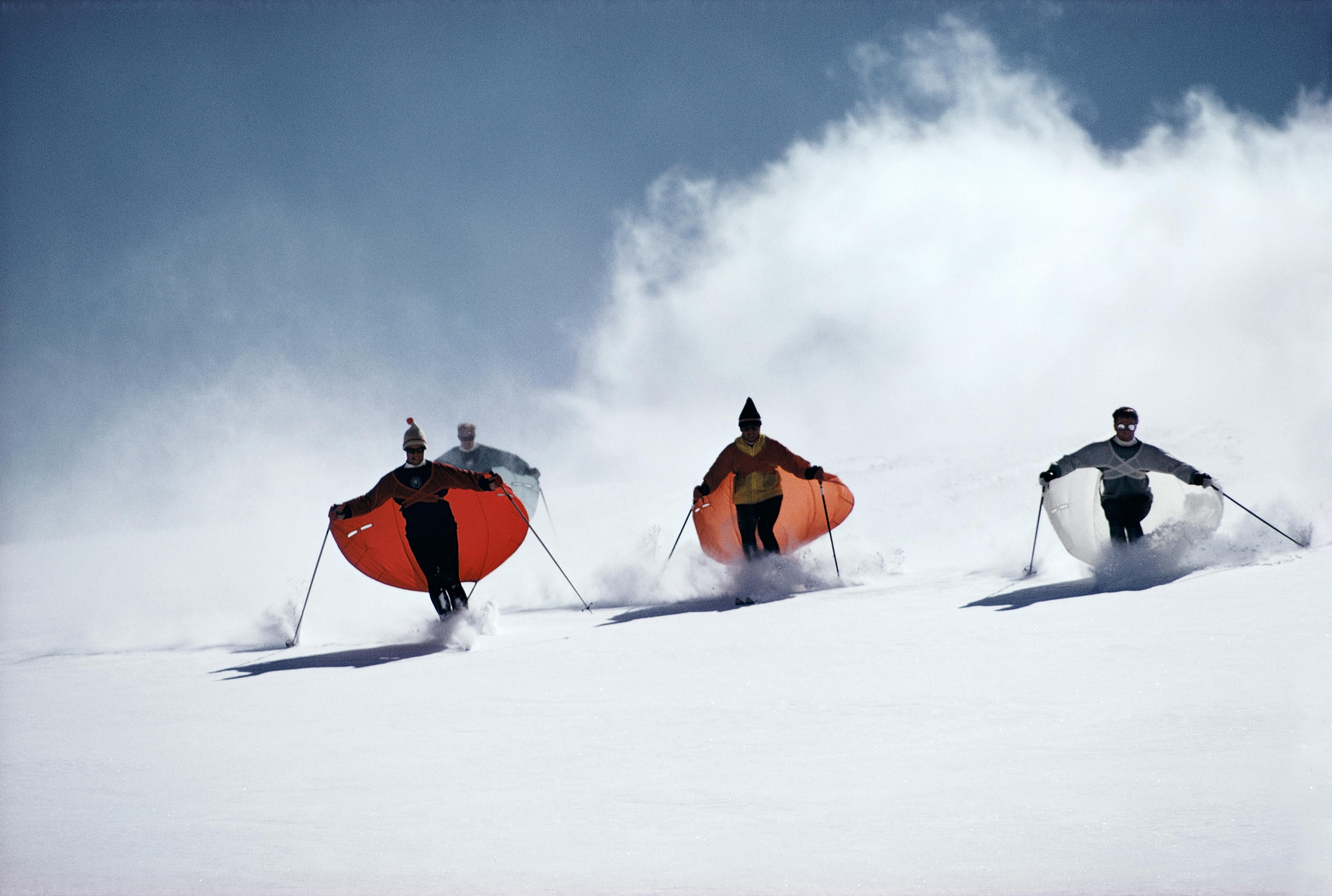 Led by skimaster Stein Eriksen, skiers 'sail' down a slope at Snowmass-at-Aspen, Colorado, circa 1967. The skiers are wearing thin capes which attach to their wrists and billow out like sails as they ski. 

Slim Aarons
Caped Skiers
1967
C print