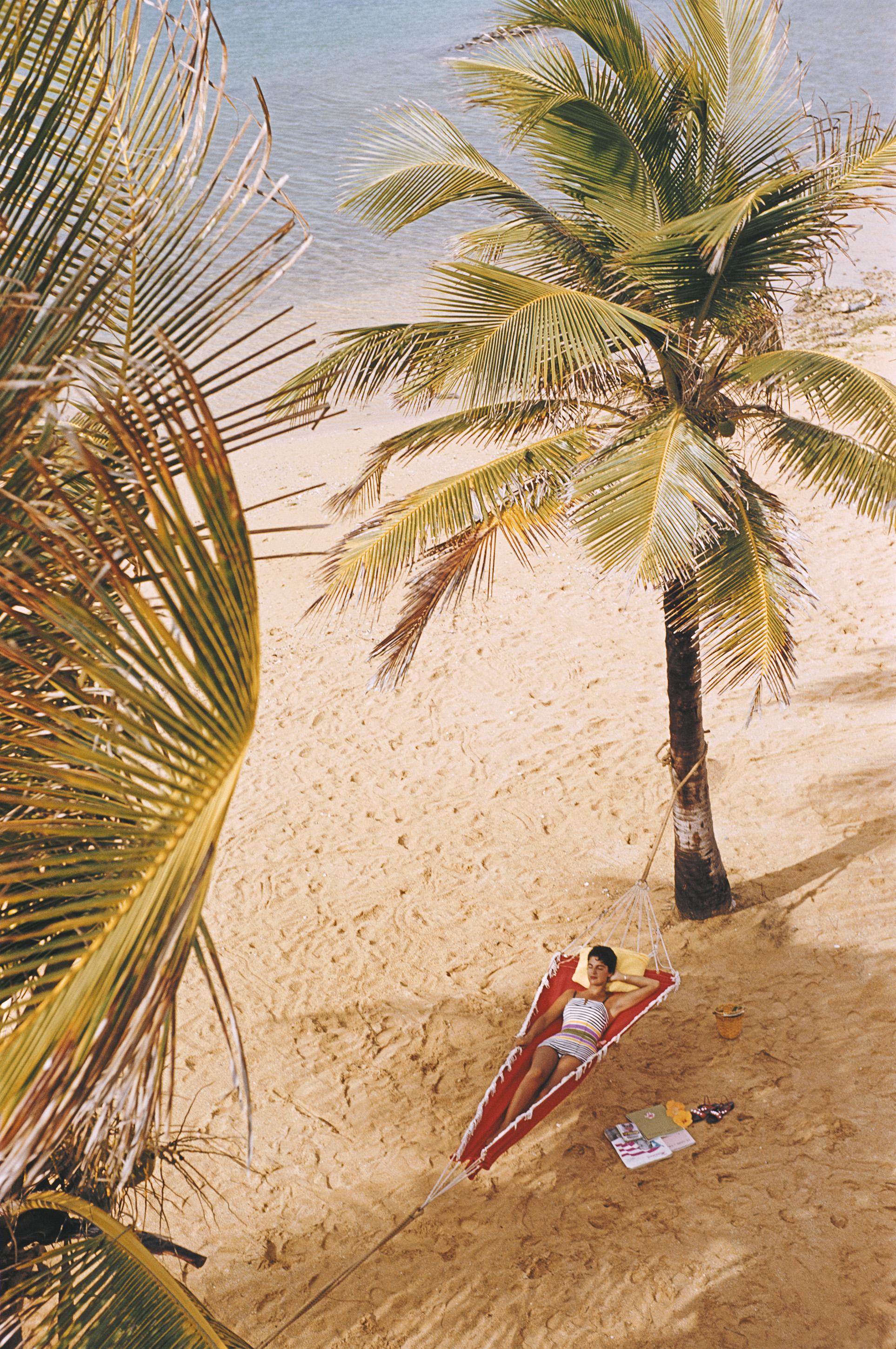 Femme allongée dans un hamac suspendu entre des palmiers sur la plage du Caribe Hilton à San Juan, Porto Rico, mars 1956.

Slim Aarons
Caribe Hilton 
1956. (imprimé ultérieurement)
C imprimé 
Édition de 150 exemplaires numérotés et estampillés par