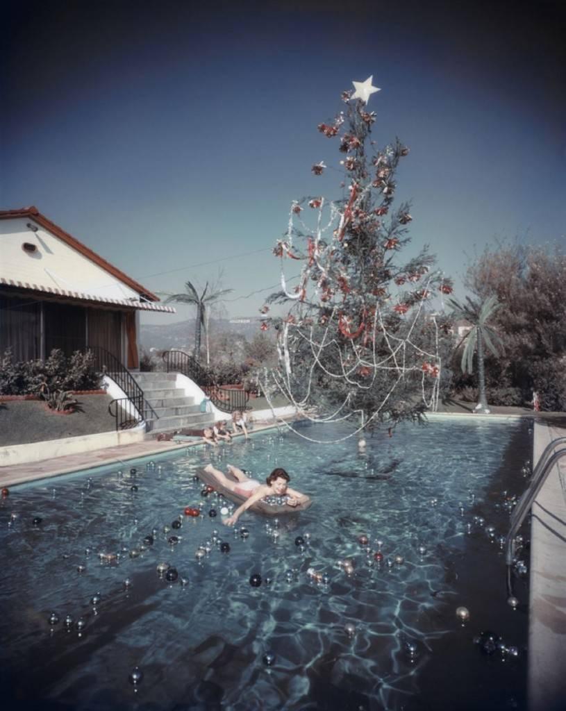 'Christmas Swim' 1954 Slim Aarons Limited Edition Estate Stamped Print
Rita Aarons, wife of photographer Slim Aarons, swimming in a pool festooned with floating baubles and a decorated Christmas tree, Hollywood, California, 1954. Two children play