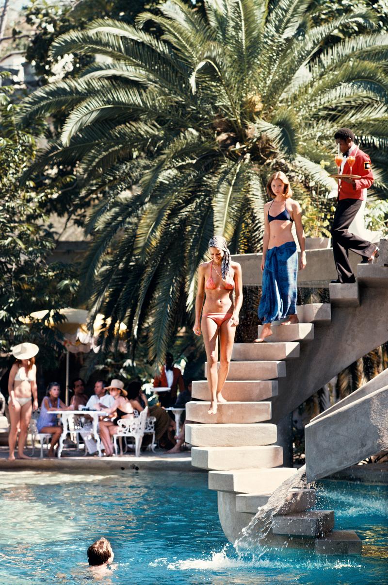 Badegäste gehen die Stufen zum Schwimmbad in der Habitation Leclerc, Haiti, Januar 1975. Ihnen folgt ein Kellner mit Cocktails.

Wunderschöner Druck im Format 60 x 40" Zoll / ca. 152 x 101 cm Papiergröße. 

Nachlassgestempelte Collection'S Ausgabe